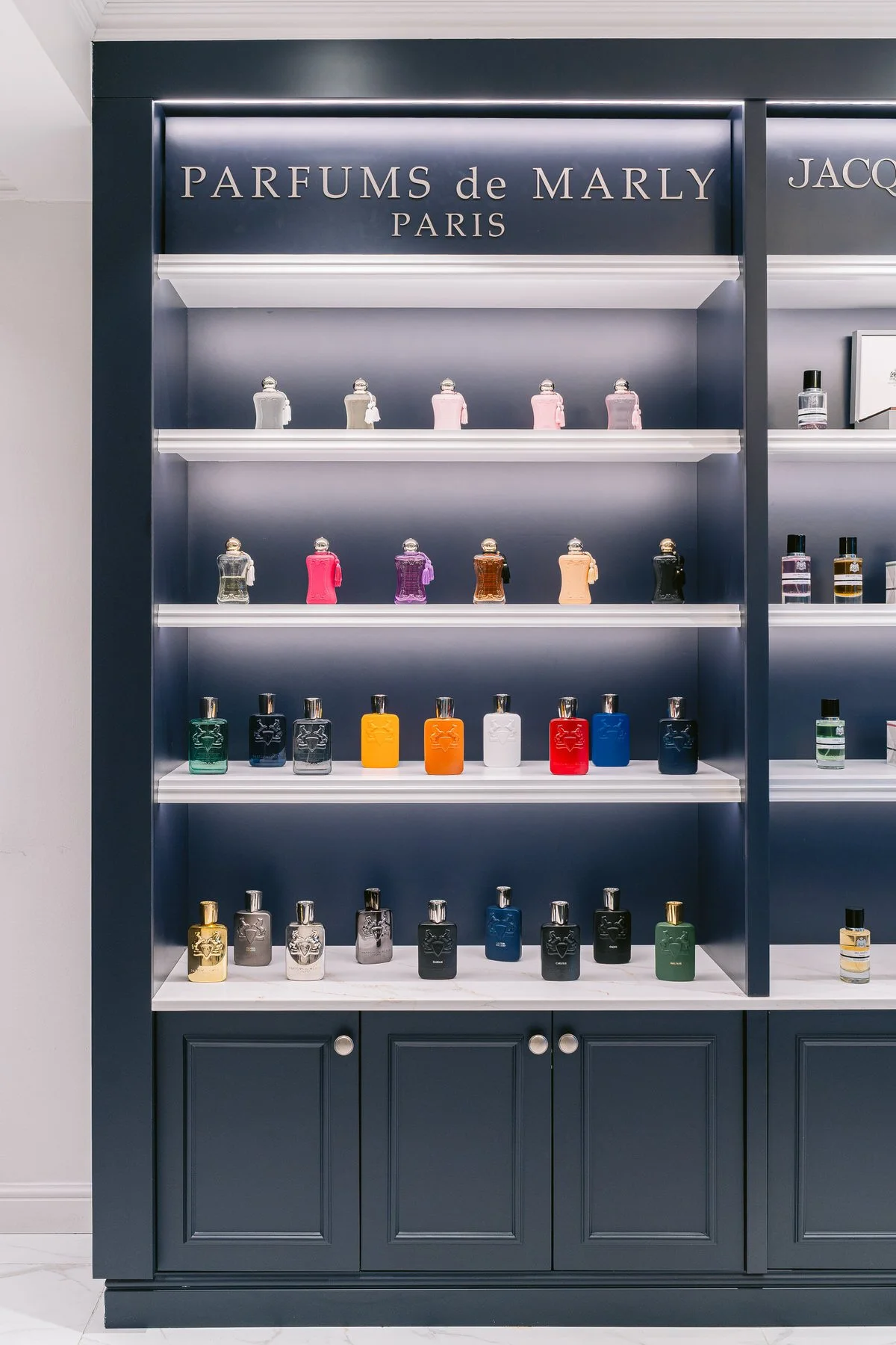 Estantería azul con diferentes frascos de perfume coloridos y una señal que dice 'PARFUMS de MARLY PARIS'.