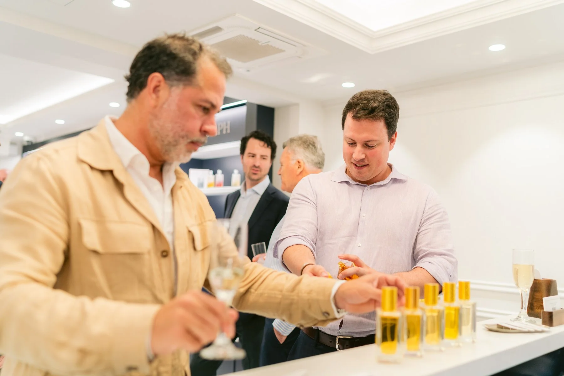 Personas en una feria o evento social, probándose productos de belleza y disfrutando de bebidas en una mesa.