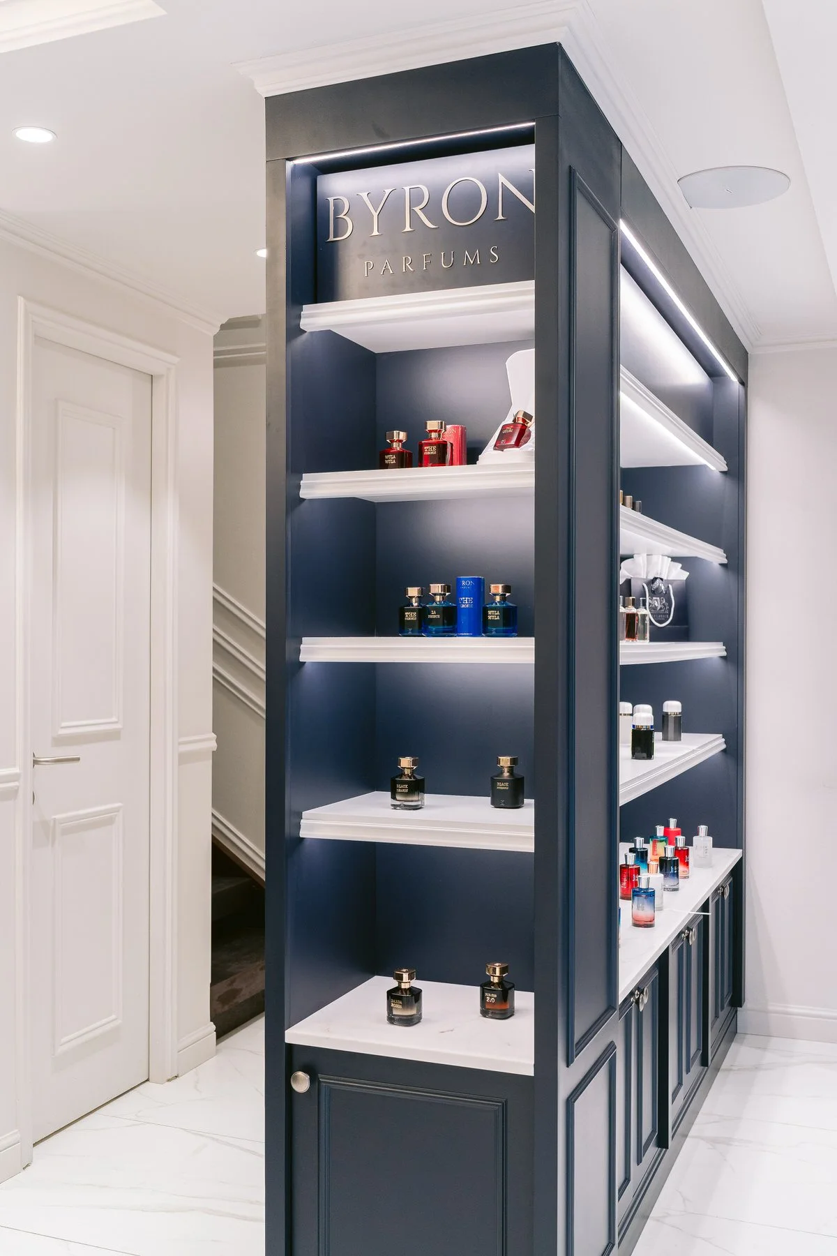 Estantería azul en una tienda de perfumes con frascos de diferentes colores y tamaños, y un cartel que dice 'BYRON PARFUMS' en la parte superior.