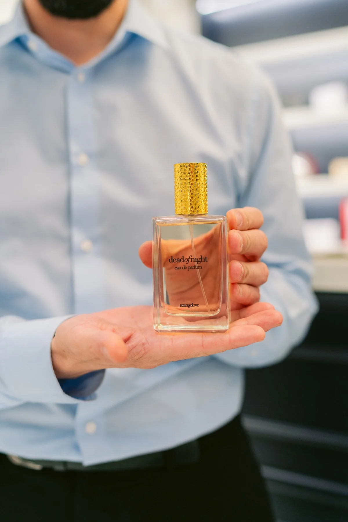 Persona sosteniendo un frasco de perfume con etiqueta que dice 'dead of night' en un entorno interior.