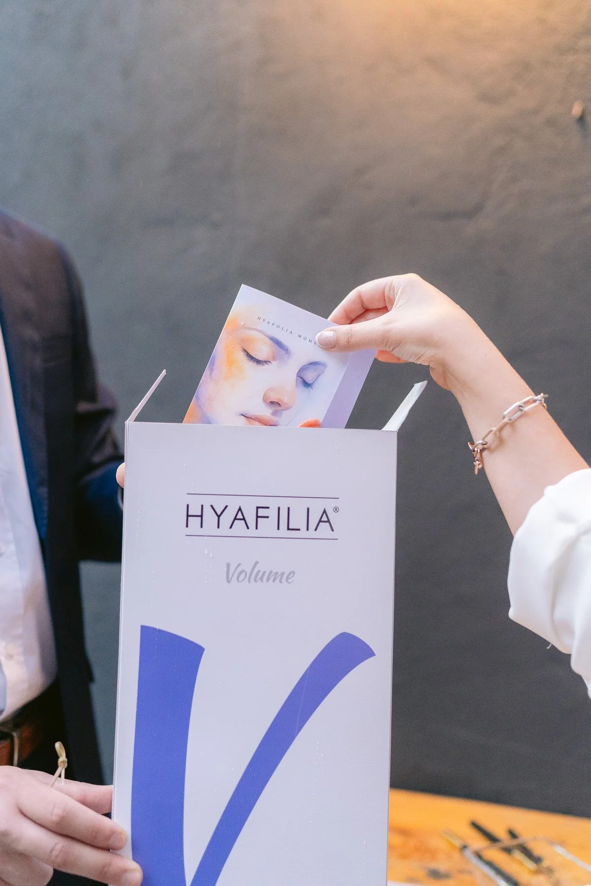Persona sacando una muestra del saco de productos Hyafilia con la etiqueta 'Volume' de un recipiente blanco.