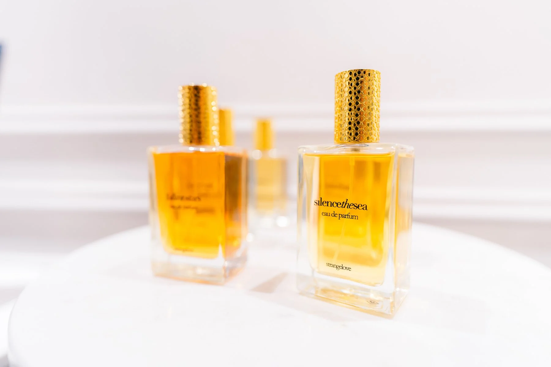 Tres frascos de perfume con líquido dorado y tapas doradas, colocados sobre una superficie blanca.