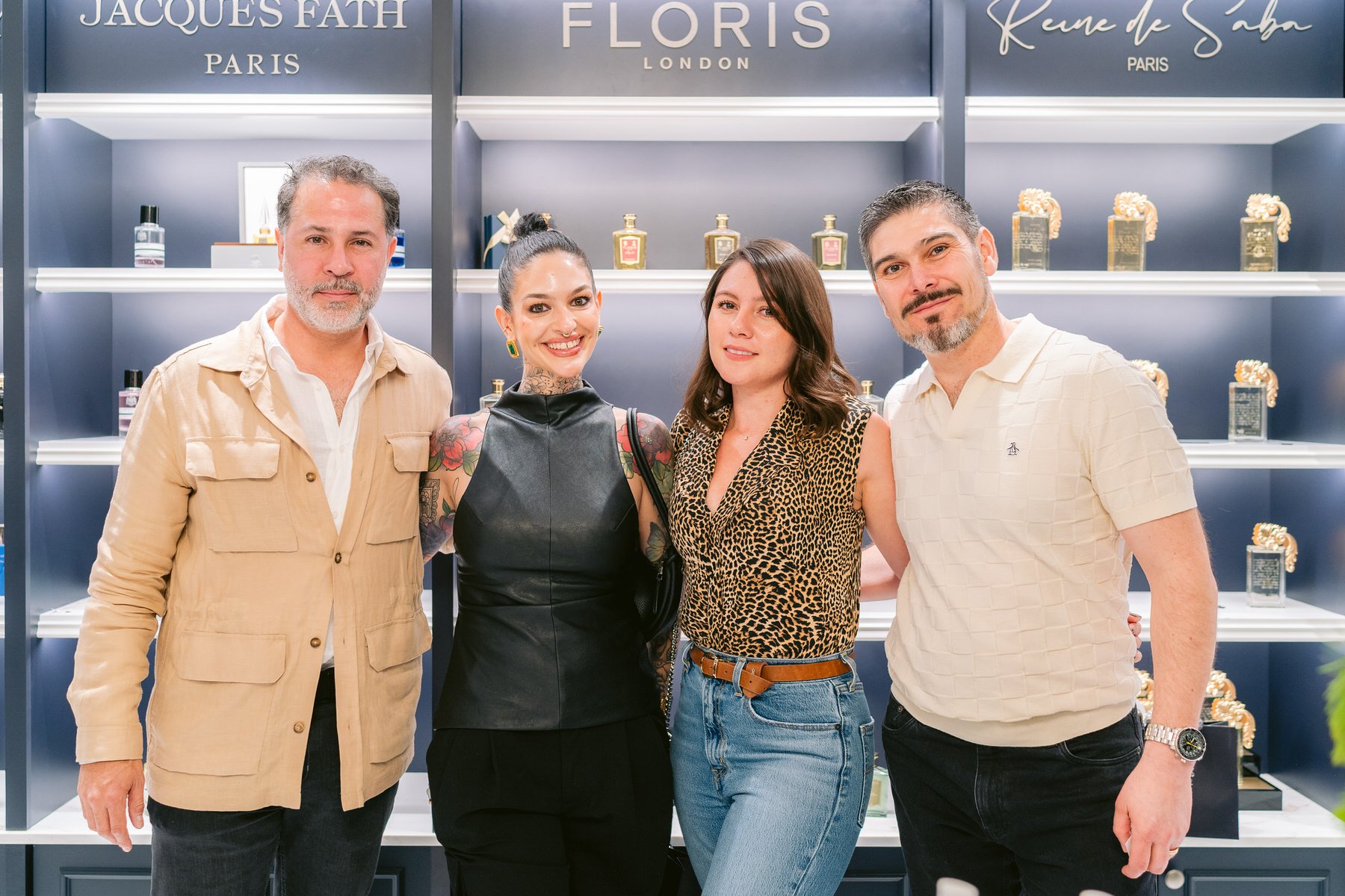 Cuatro personas de pie en frente de estantes con perfumes y productos de belleza, en un fondo de color gris y azul. 