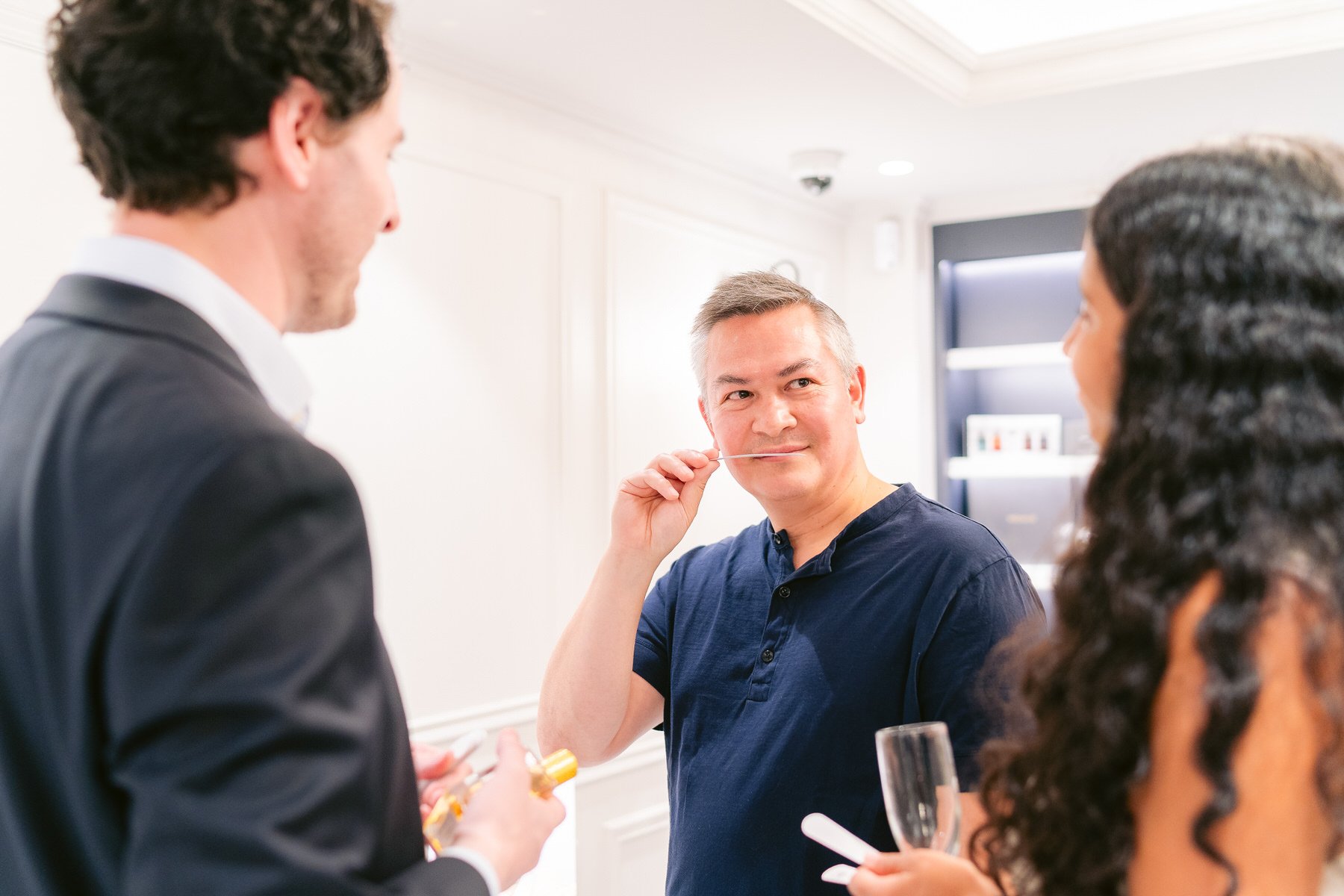 Tres personas en una fiesta, una de ellas con una pipa en la mano y una copa, en una sala decorada con colores claros.