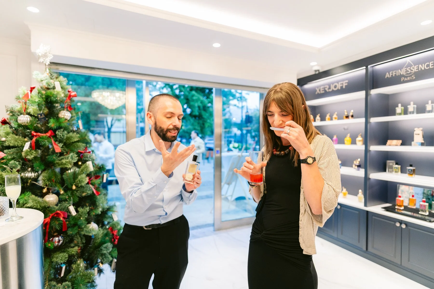 Dos personas en una tienda de perfumes, una mujer oliendo una muestra y un hombre explicando.»
