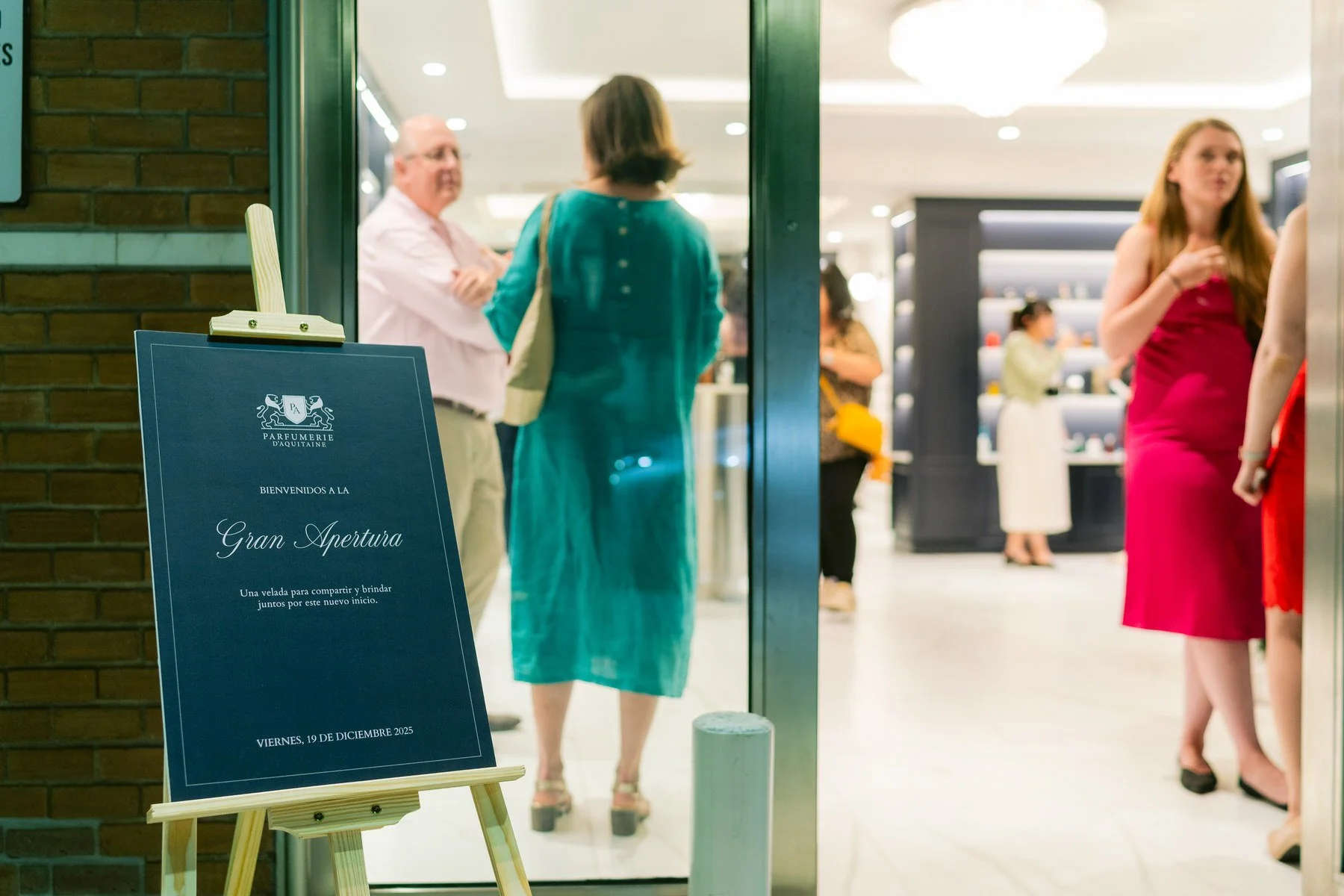 Cartel de bienvenida a la apertura de una tienda, con texto en español y personas conversando en el interior.
