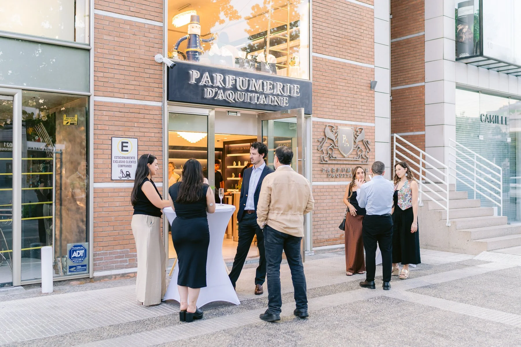 Grupo de personas conversando en la entrada de una perfumería llamada Parfumerie d'Aquitaine, en un entorno urbano.