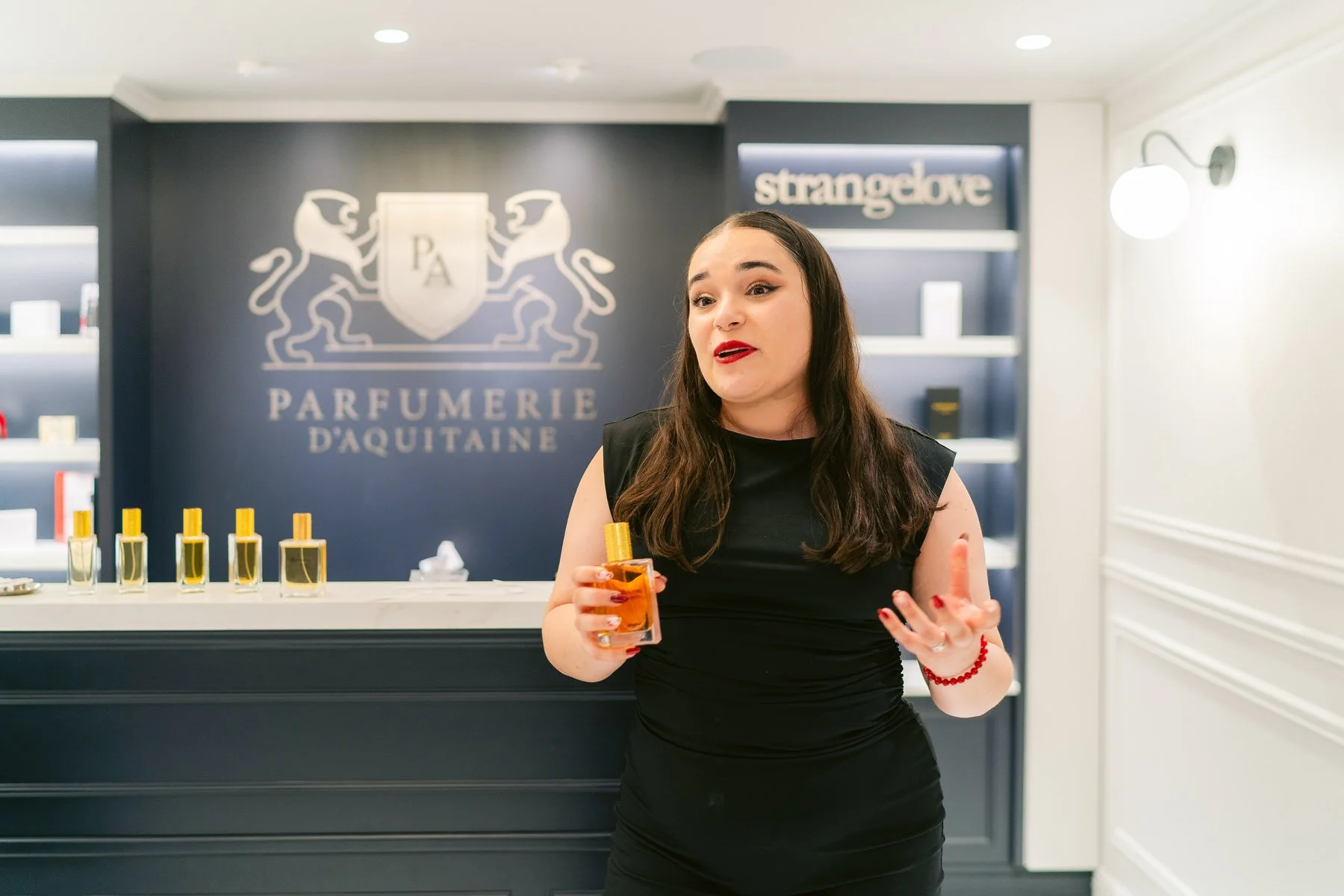 Mujer en una tienda de perfumes D'Aquitaine hablando y sosteniendo una botella de perfume con líquido naranja