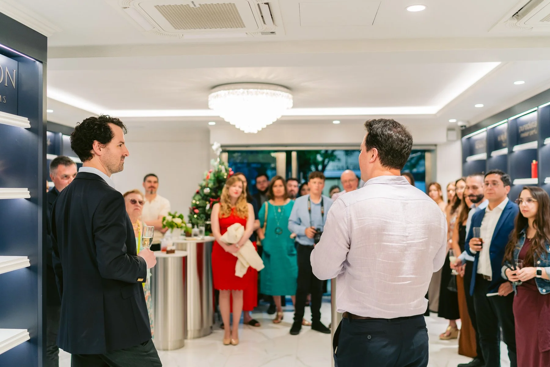 Un grupo de personas en una fiesta o evento social en un lugar elegante con decoración navideña, atendiendo a un orador o presentador.