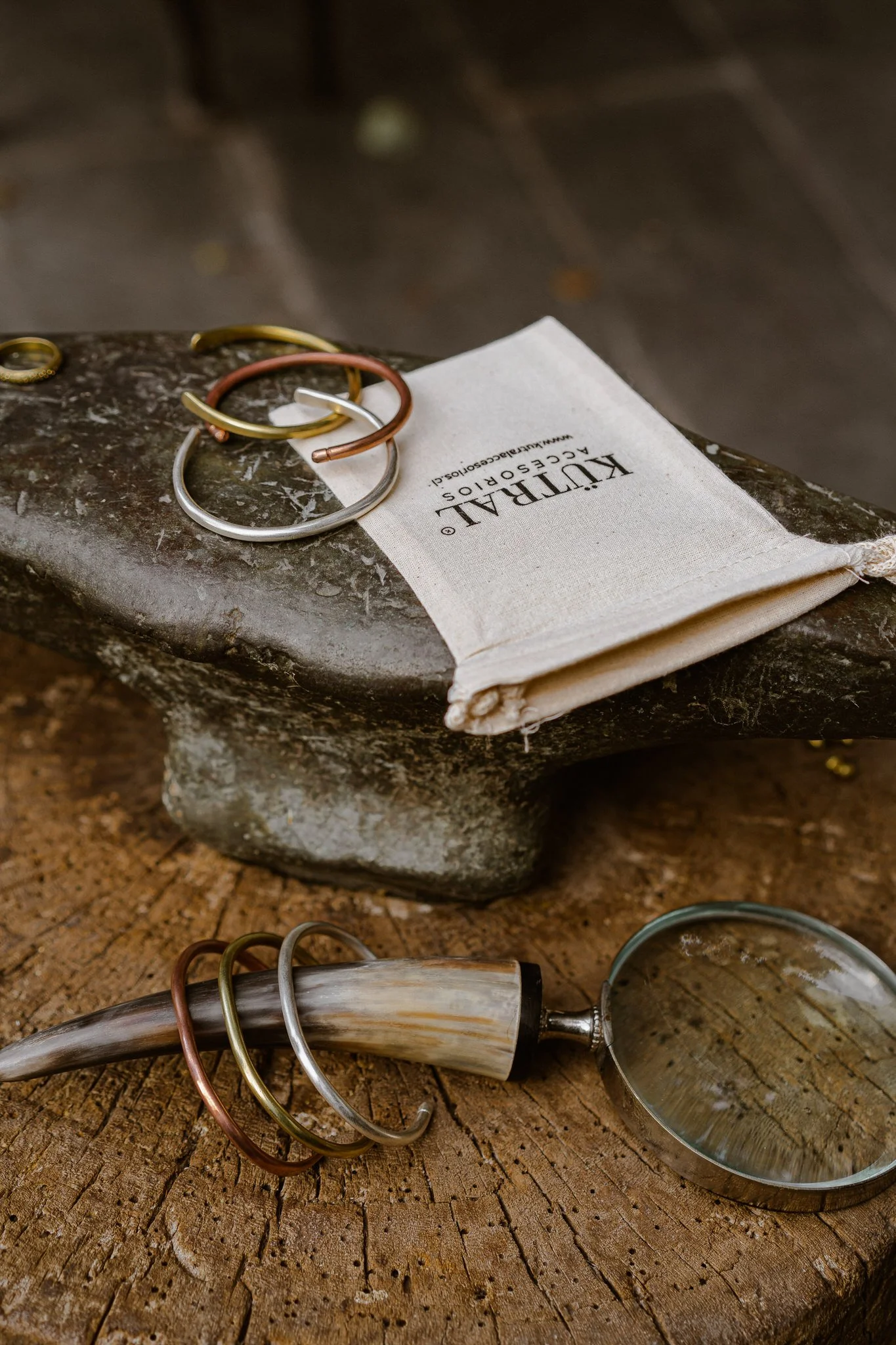 Varios anillos de diferentes colores colocados sobre una piedra y un buril con lupa en una mesa de madera.