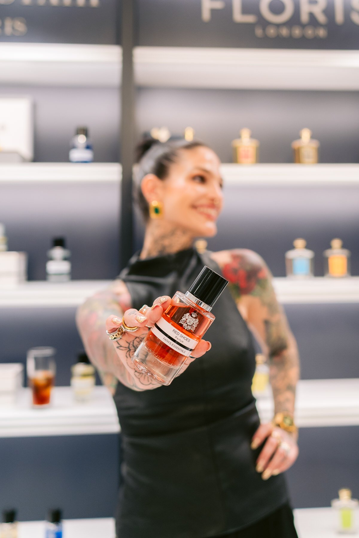 Mujer con tatuajes sosteniendo un frasco de perfume con despacio en una tienda de perfumes