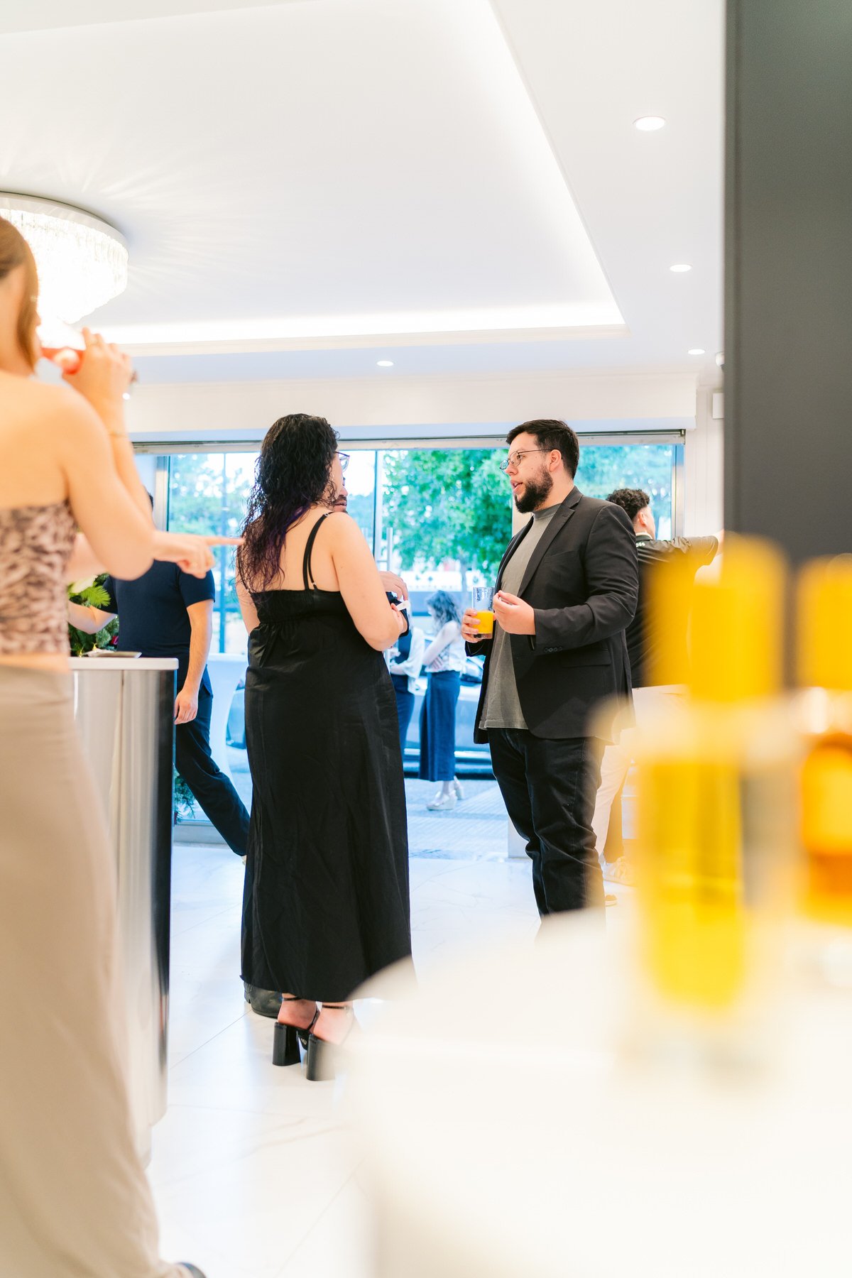 Personas conversando en un evento social en interiores con ventanas grandes y vista a un área exterior