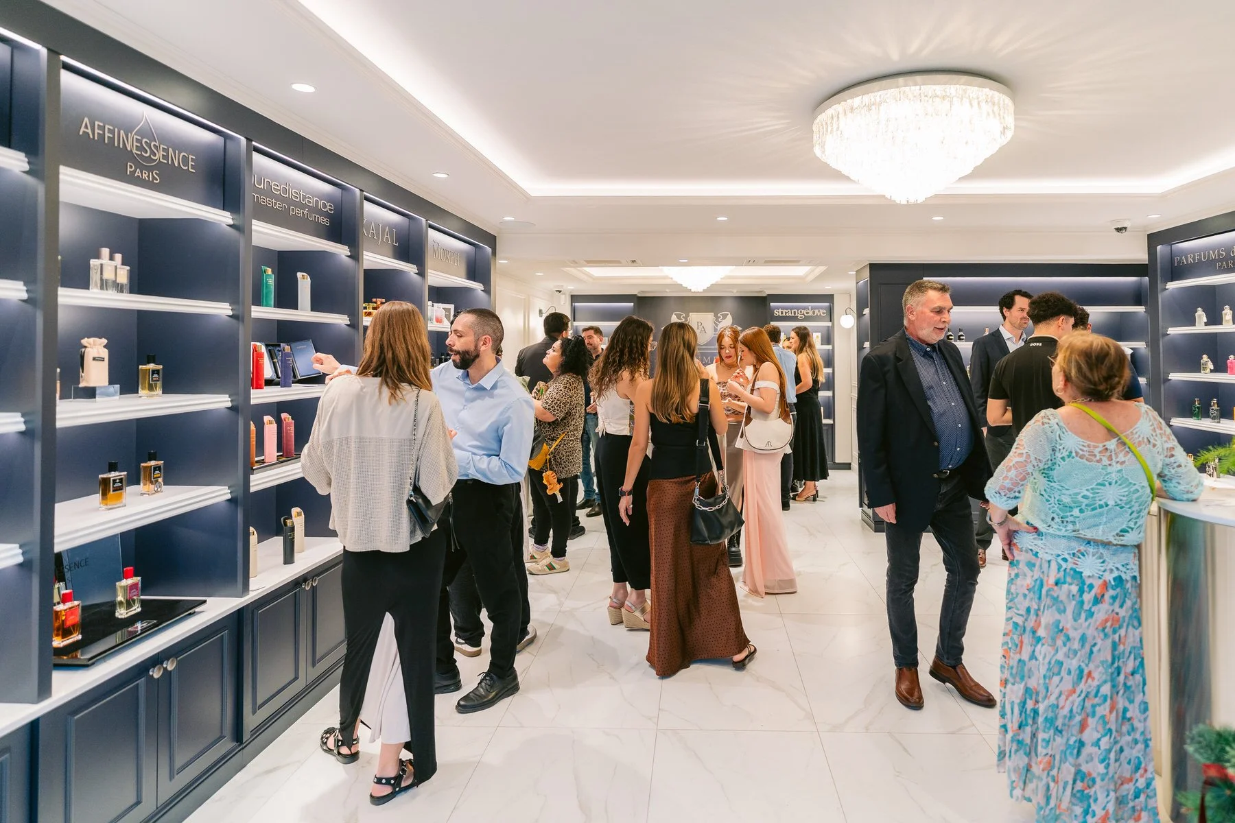 Clientes en una tienda de perfumes, algunos viendo frascos en las estanterías y otros hablando con el personal, en un entorno elegante y bien iluminado.