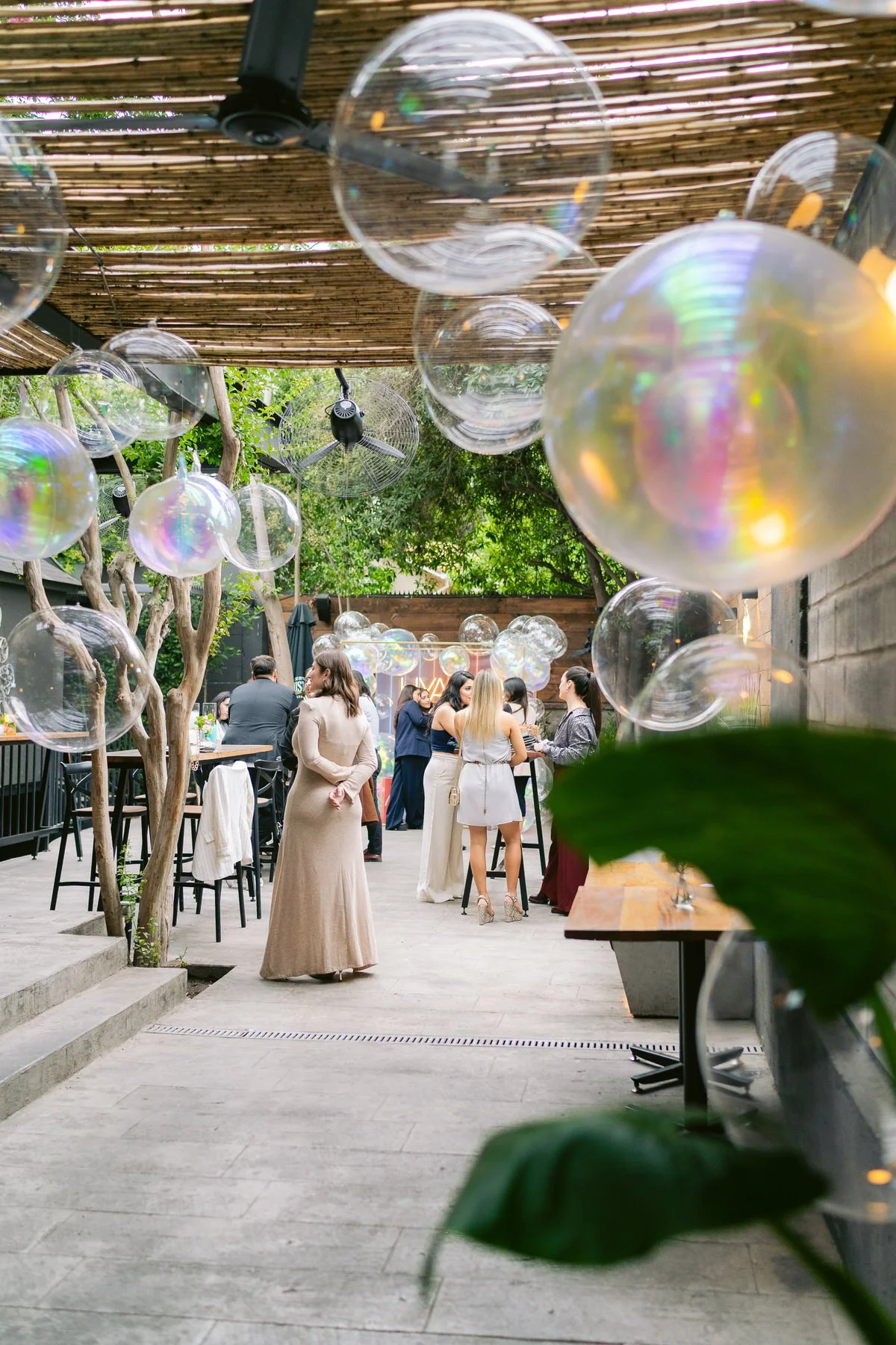 Evento social con personas conversando en un espacio al aire libre decorado con bolas de jabón flotando.