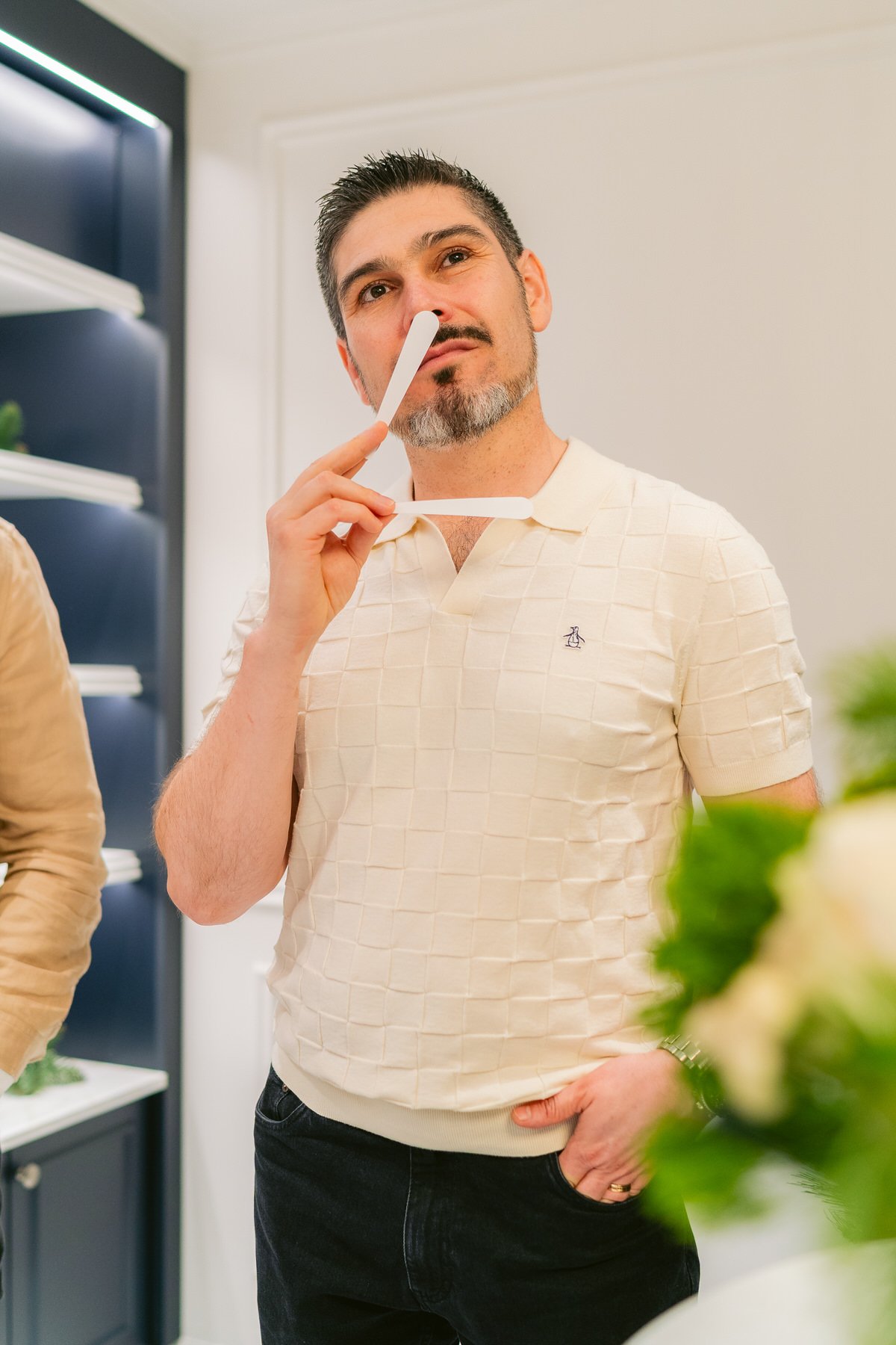 Hombre con barba, vestimenta casual, sosteniendo un palillo de prueba junto a la nariz en un ambiente interior.