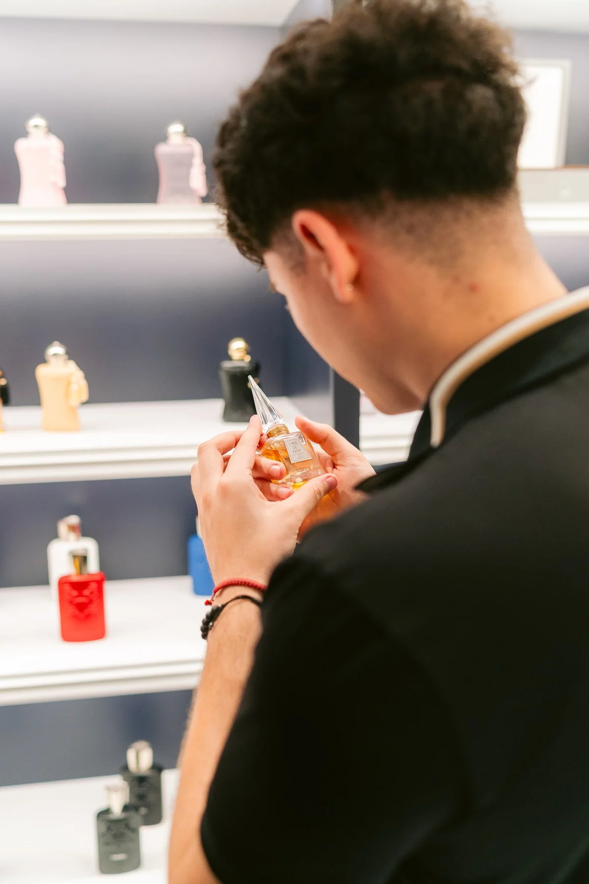 Joven en una tienda de perfumes, inspeccionando una botella de perfume.