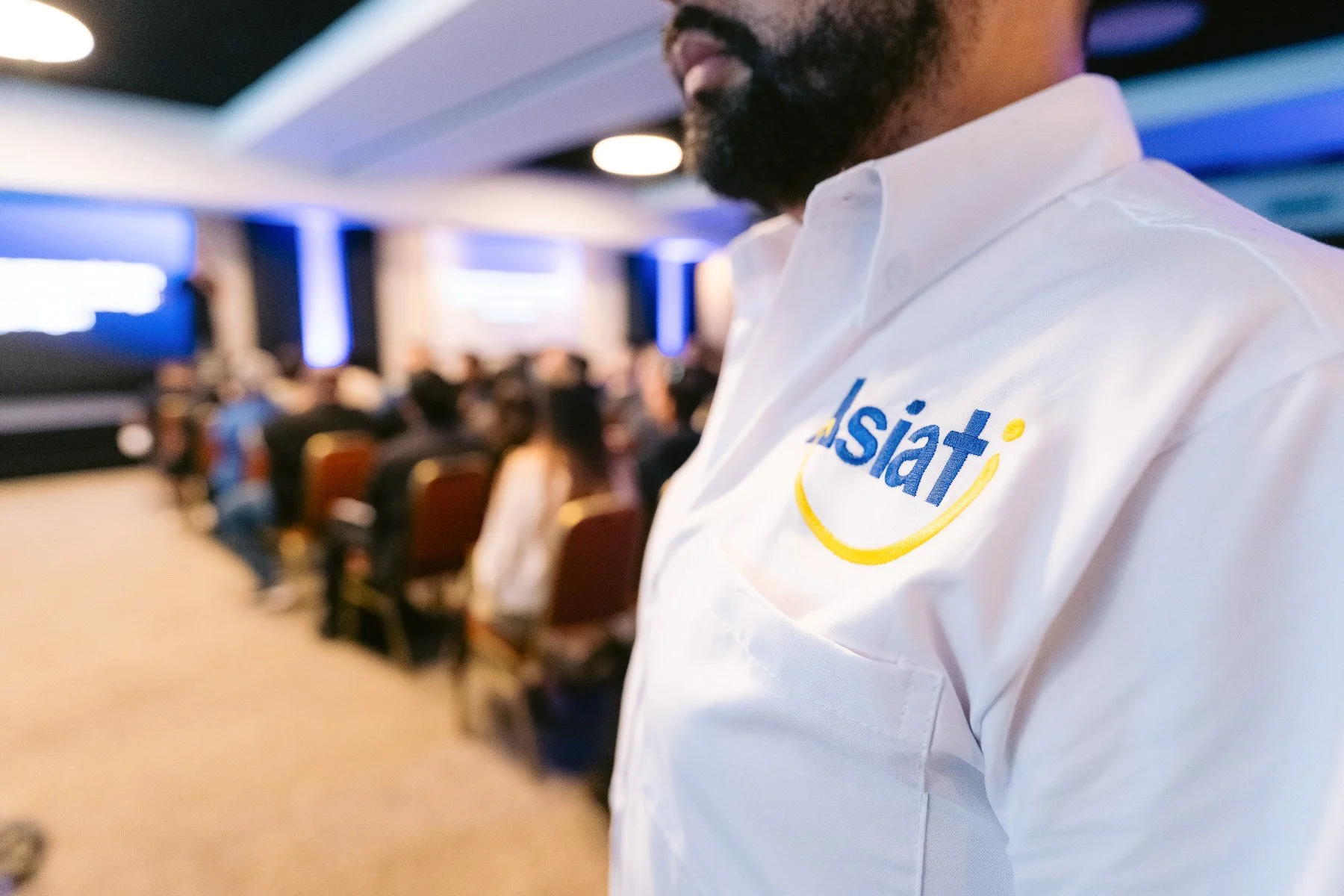 Persona con camiseta blanca con logotipo de Asiat en un evento con audiencia en el fondo.