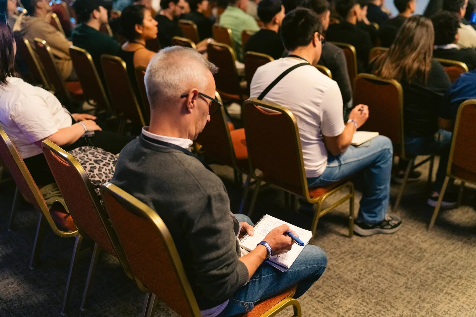 Varias personas sentadas en sillas durante una conferencia, atendiendo y tomando notas.