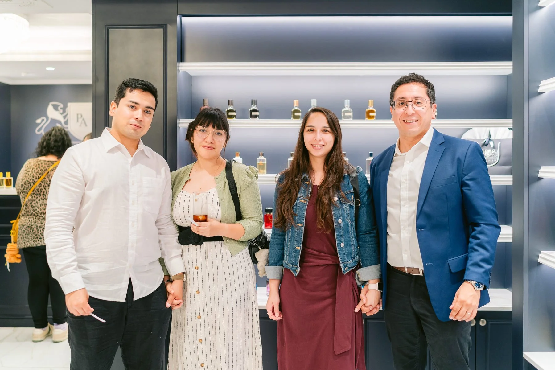Cuatro personas de pie en una tienda, son dos hombres y dos mujeres, todos sonriendo y luciendo elegantes, en el fondo hay estantes con botellas.