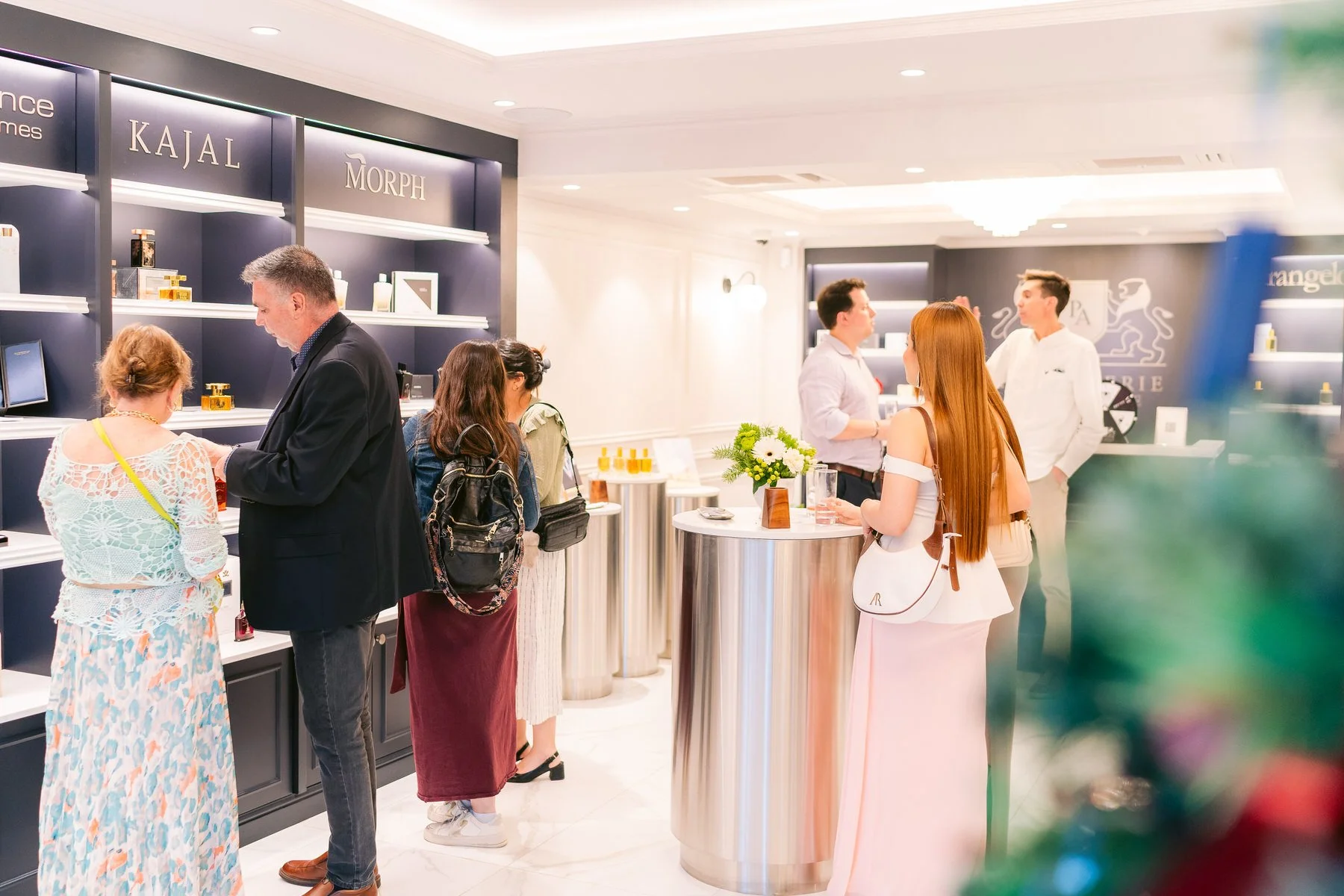 Personas en una tienda de belleza o farmacia observando productos y conversando con empleados en un ambiente moderno y bien iluminado.