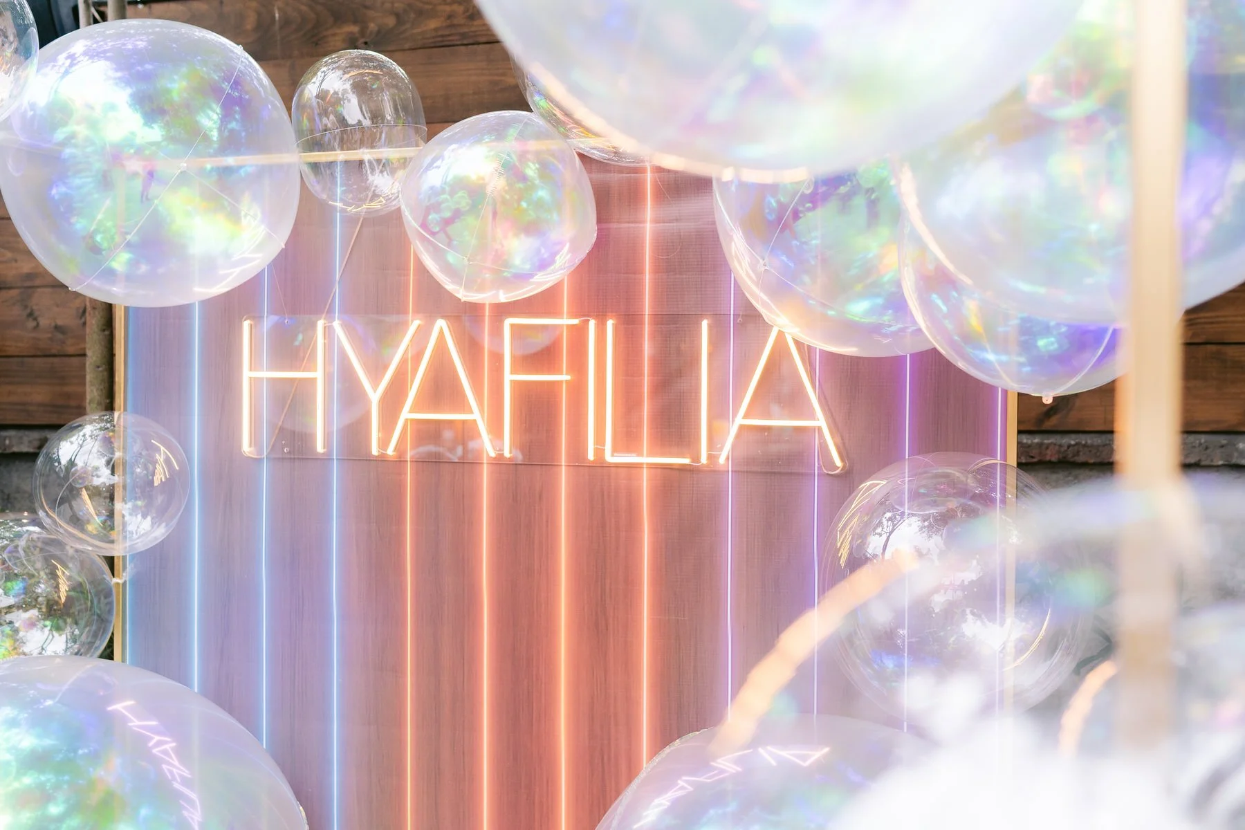 Decoración con globos transparentes y neón que dice 'HYALIA' en un fondo de madera con luces de neón.