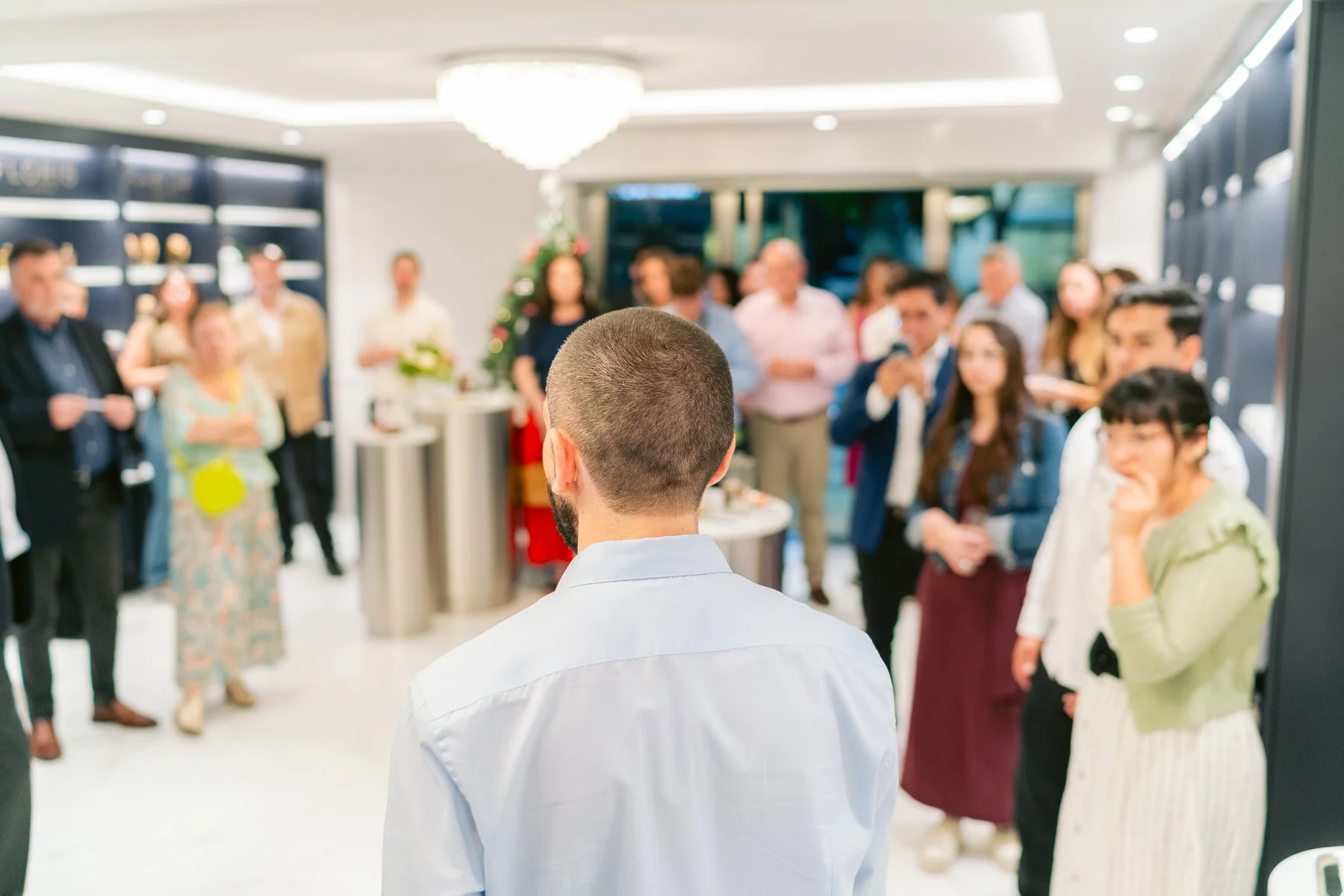 Hombre con barba y cabello corto de espaldas en una fiesta con muchas personas en un ambiente elegante.
