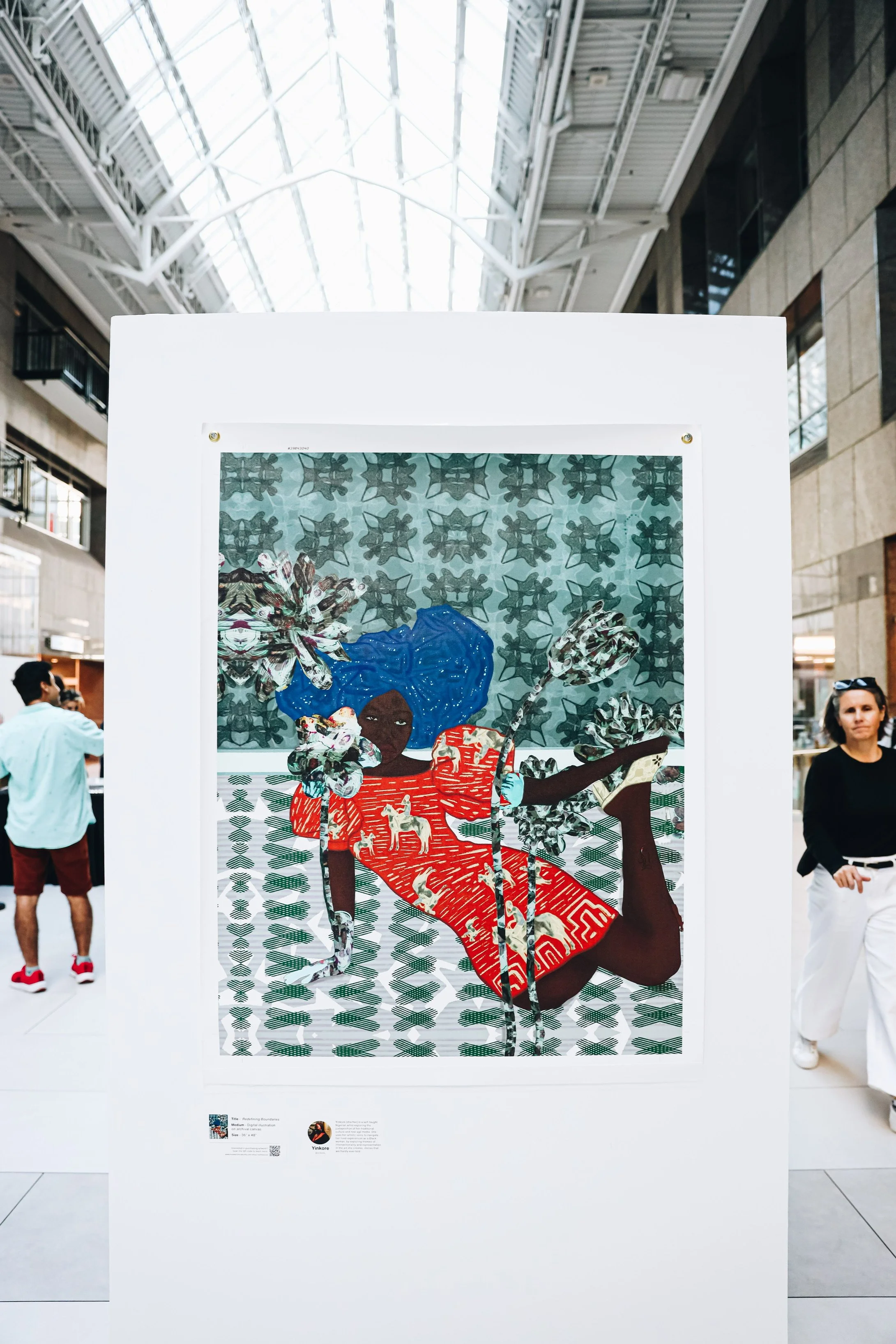 Art installation of a woman with blue hair, sitting with one leg crossed and one leg extended, wearing a red dress with dog patterns, set against a patterned background, on display in a spacious interior.