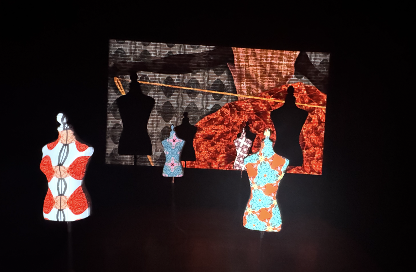 Display of fashion mannequins with colorful patterned fabrics against a digital backdrop of abstract patterns and red textured landscapes.