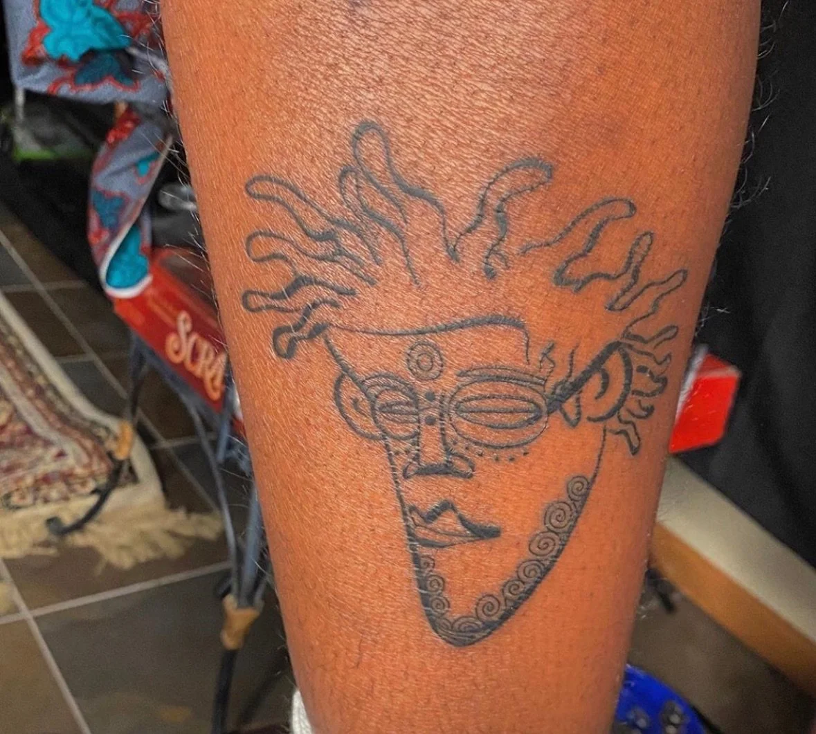 Tattoo of a smiling face with curly hair and earrings on a person's arm.