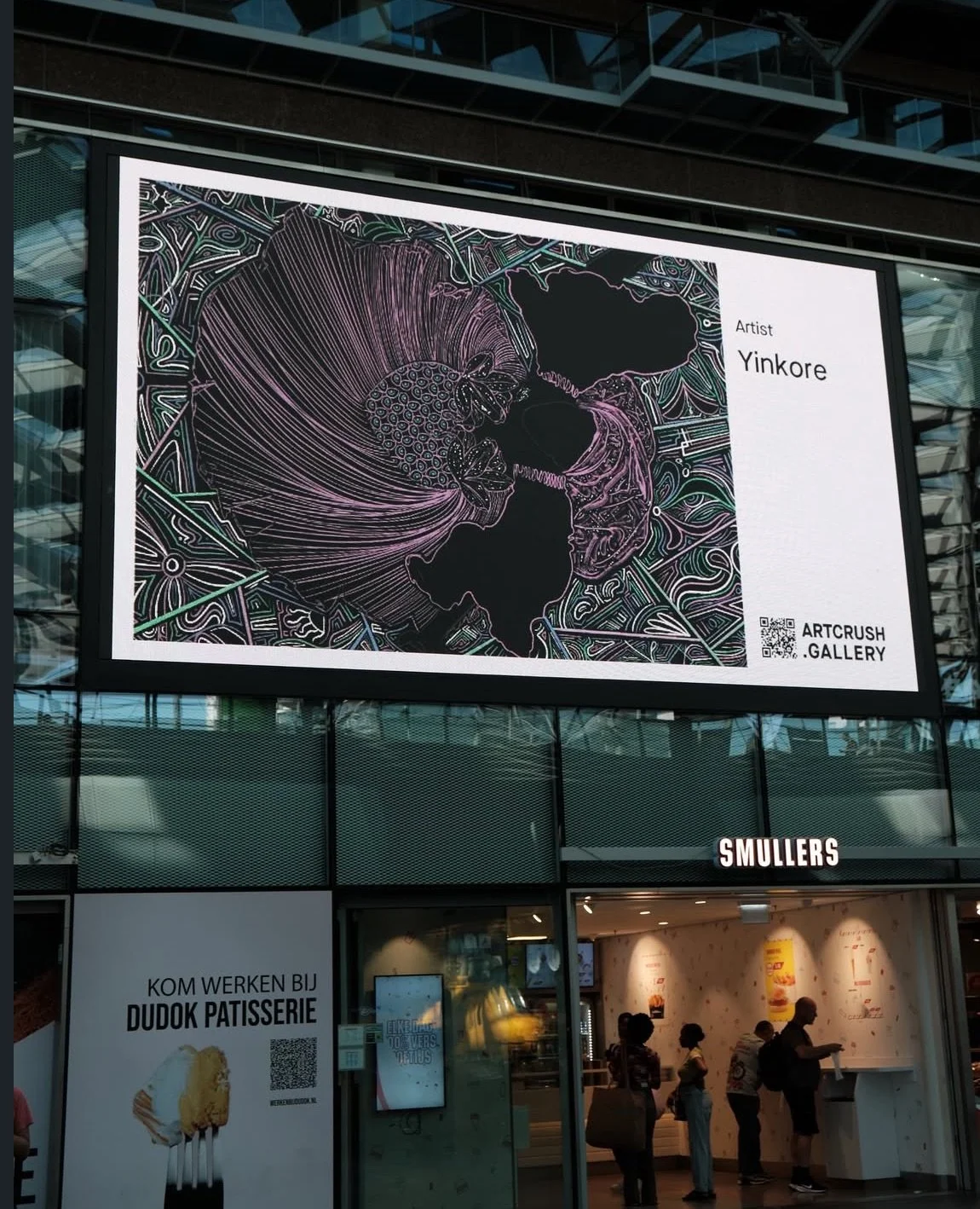 Digital billboard displaying an art piece titled 'Yinkore' by ARTCRUSH GALLERY, with a QR code. The artwork features abstract, line-drawn floral or botanical elements in vibrant colors on a dark background.