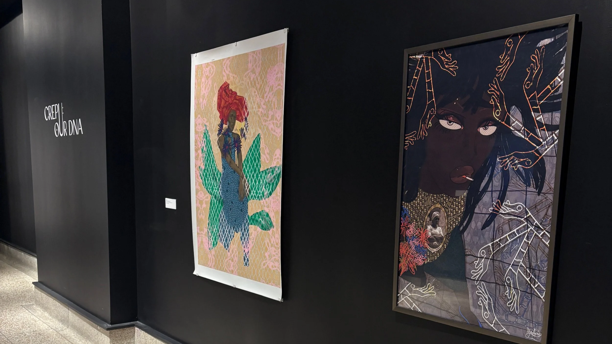 Art exhibit featuring two colorful portraits of women, one with red hair and blue outfit and the other with dark skin and braided hair, displayed on a black wall, with the text 'CREPI: OUR DNA' on the left.