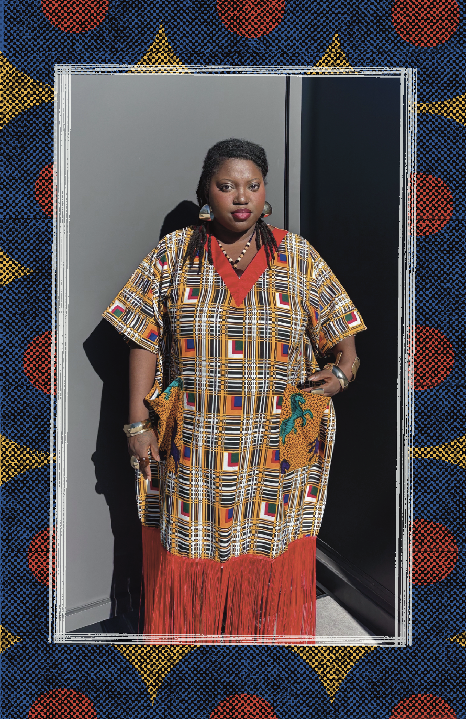 A woman wearing a colorful, patterned dress with a red fringe at the bottom, posing with her hand on her hip against a plain gray background. She is accessorized with large earrings, bracelets, and rings.
