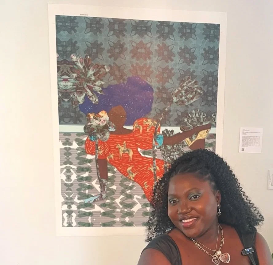 A woman with curly black hair and jewelry is taking a selfie in front of an artwork depicting a girl in a red dress with a horse pattern, sitting on a patterned floor with a dark background.