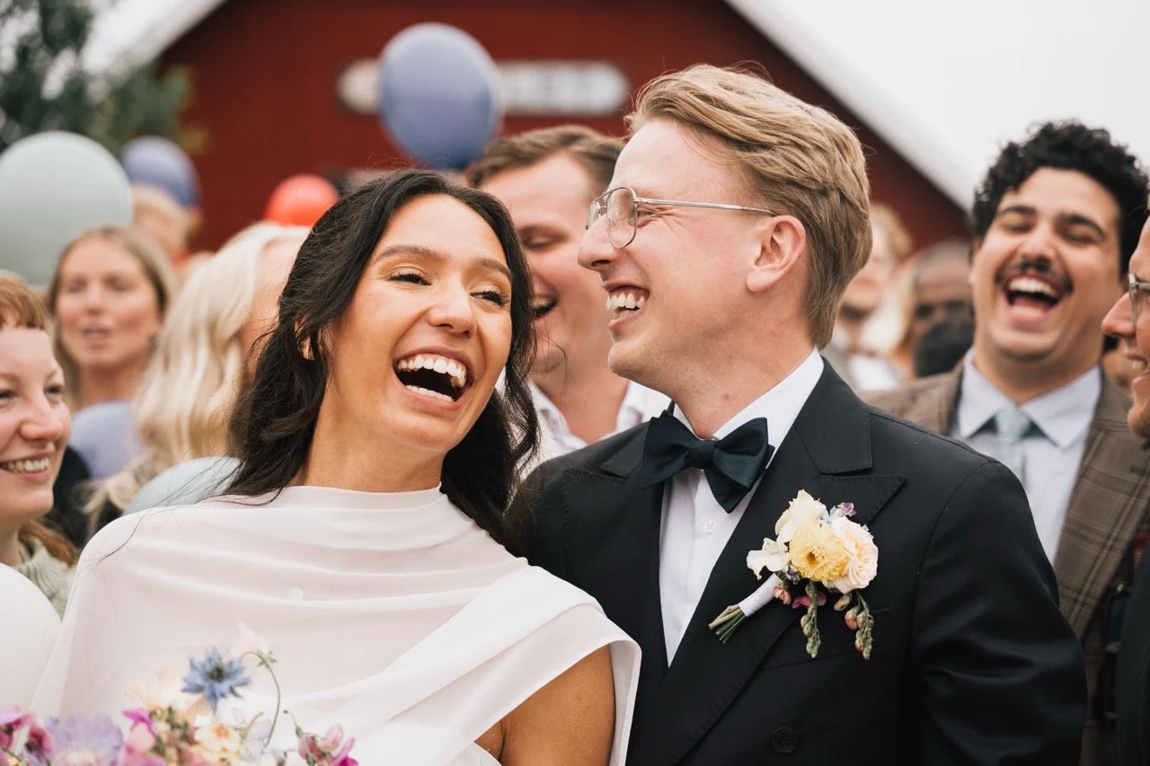 En nygift brud och brudgum ler mot varandra på ett bröllop, omgivna av gäster och ballonger.