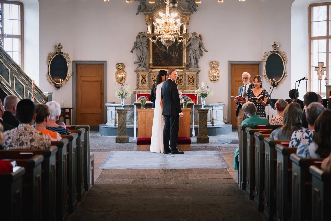 Ett brudpar som står framför präster och välsignas i en kyrka under ett bröllop.