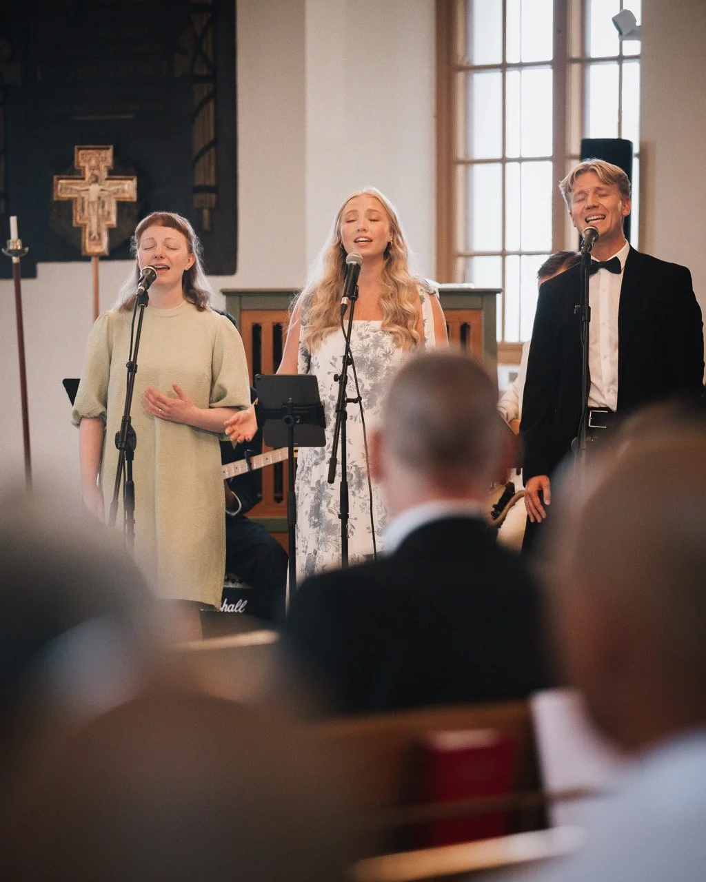 Tre personer som sjunger i kyrkan, två kvinnor och en man, med publik i förgrunden.