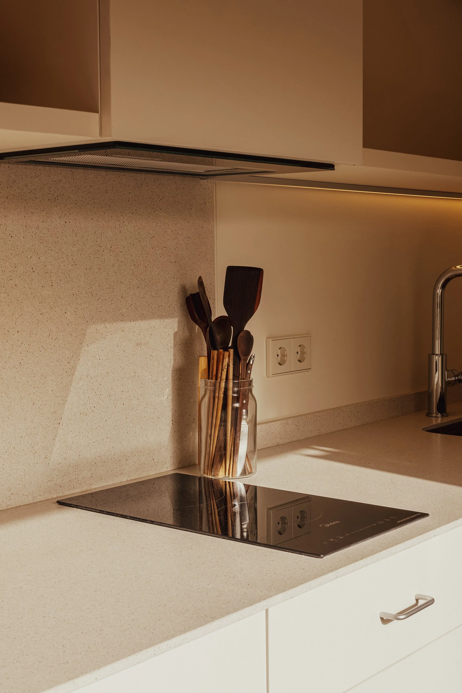 Kitchen countertop with a jar of wooden and black plastic utensils, electric stove, and a sink with a faucet.