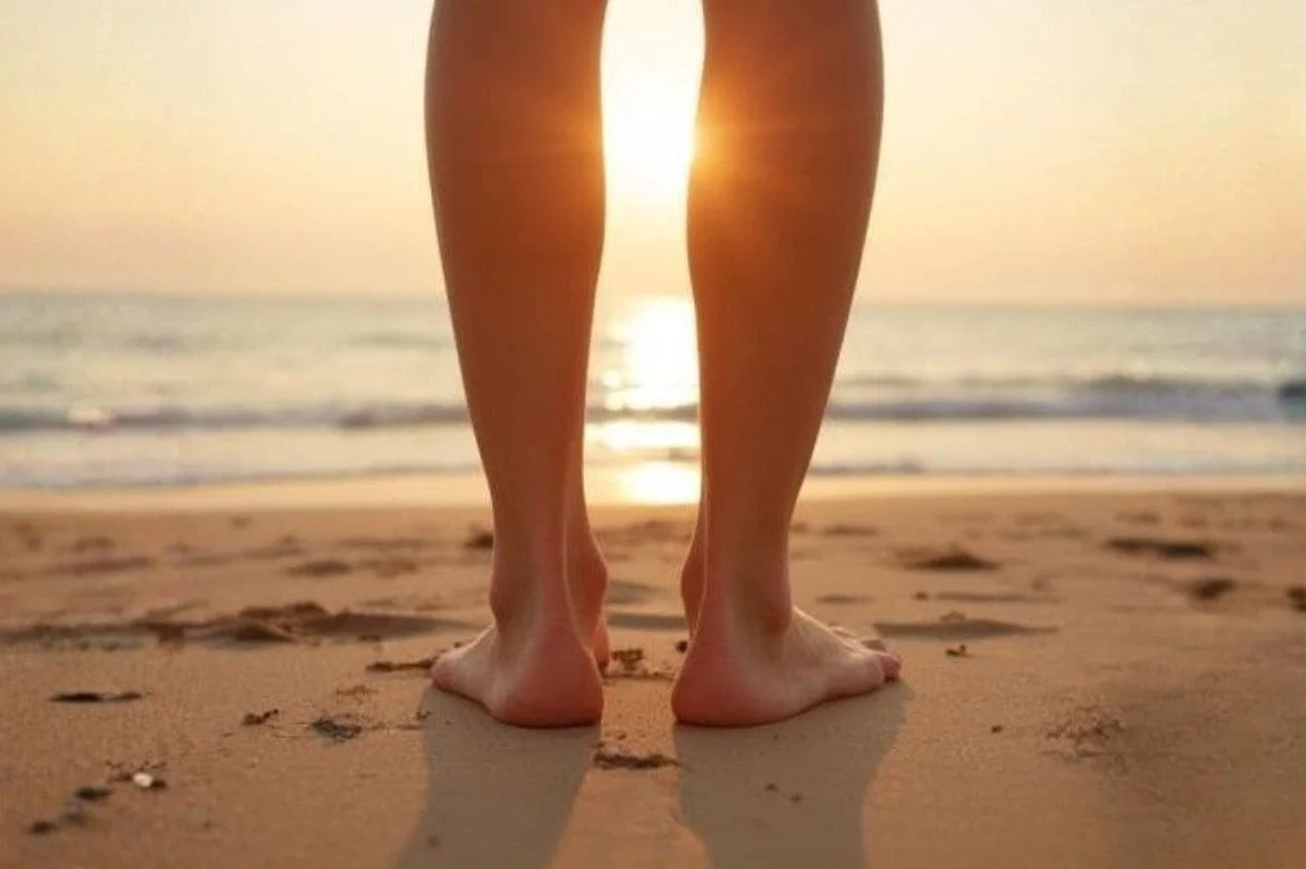 Zwei Füße auf Sandstrand, Meer und Abendsonne im Hintergrund. Moment der Zentrierung, Erdung und inneren Ruhe