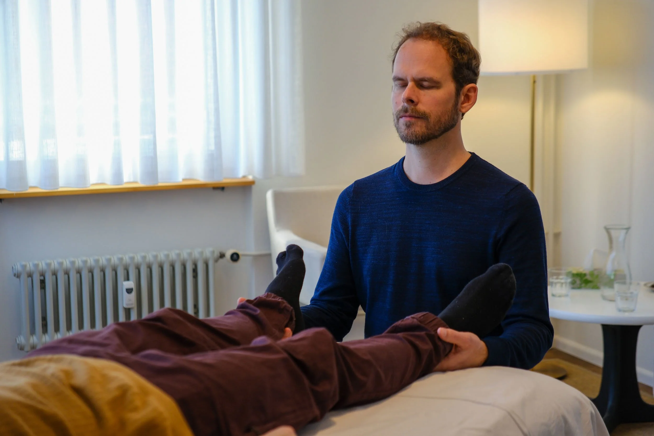 Adam Sippola hold the feet of a client during a Presence Touch session in the bright practice room of Crossover Integrative Arts.