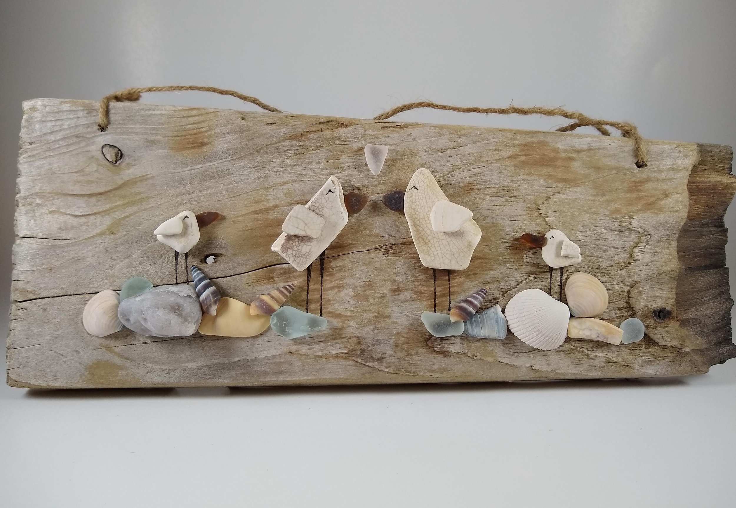 This plank is host to an entire beach scene filled with pottery birds, beach glass, stone and shells.