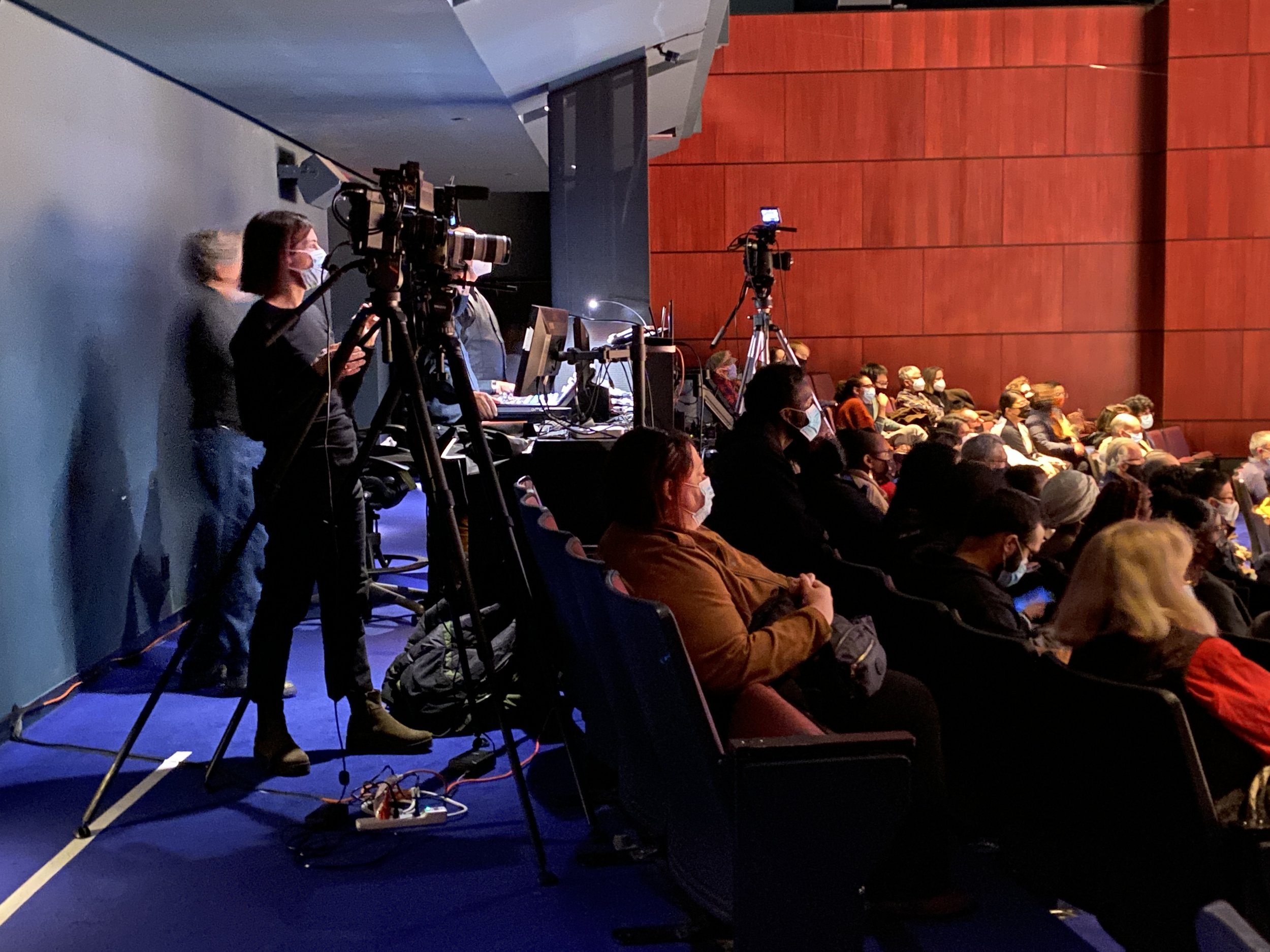 A woman films the ensembles with a large standing video camera during a concert Taplin Auditorium.