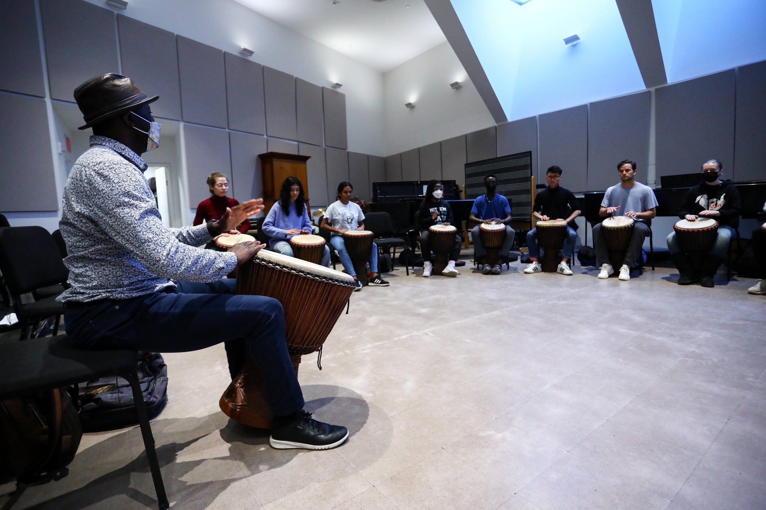 Olivier addresses his ensemble while sitting with a drum during rehearsal.