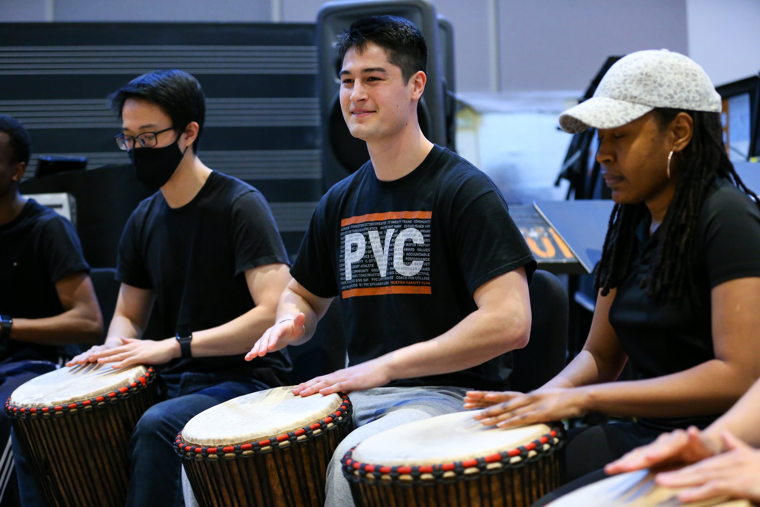 A student smiles while playing the djembe drum in a Woolworth Center classroom.