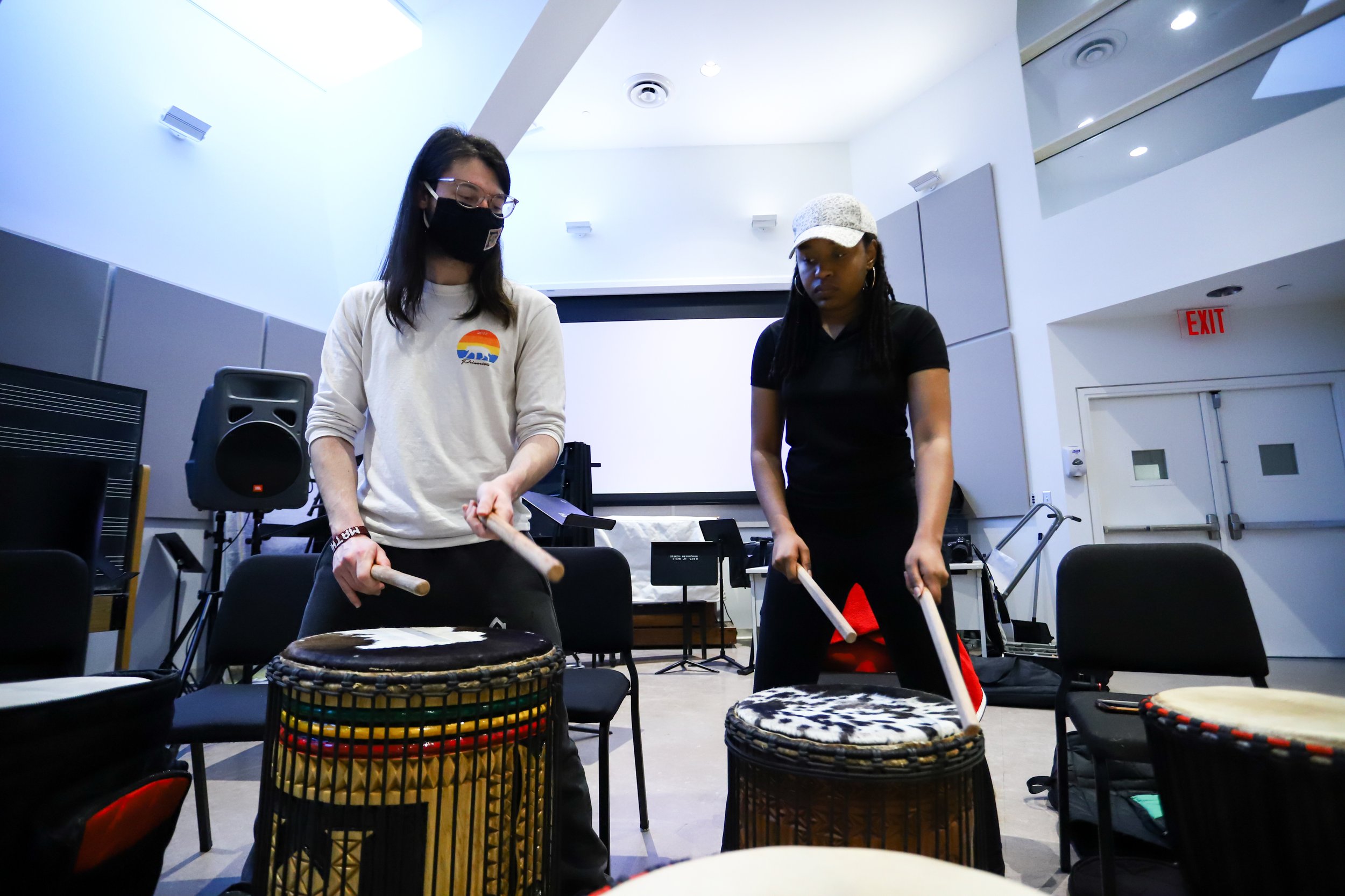 Students play the djembe drum with drumsticks in a Woolworth Center classroom.