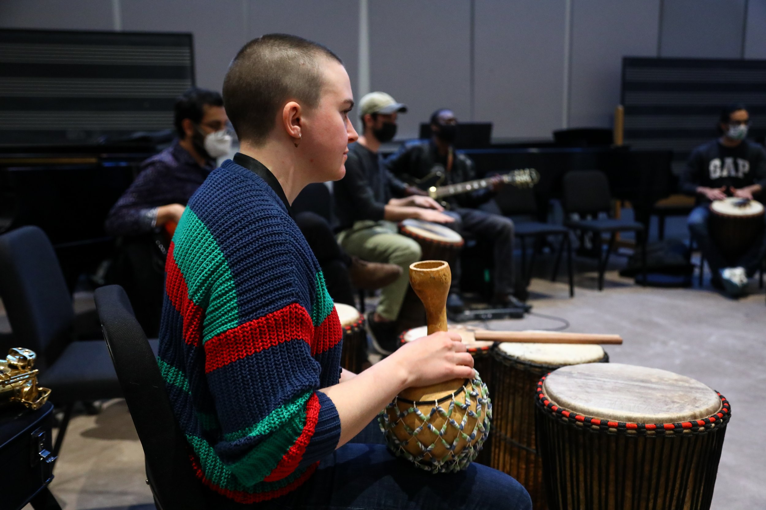 A student listens to Olivier's direction while holding a shekere, an instrument made from a dried gourd.