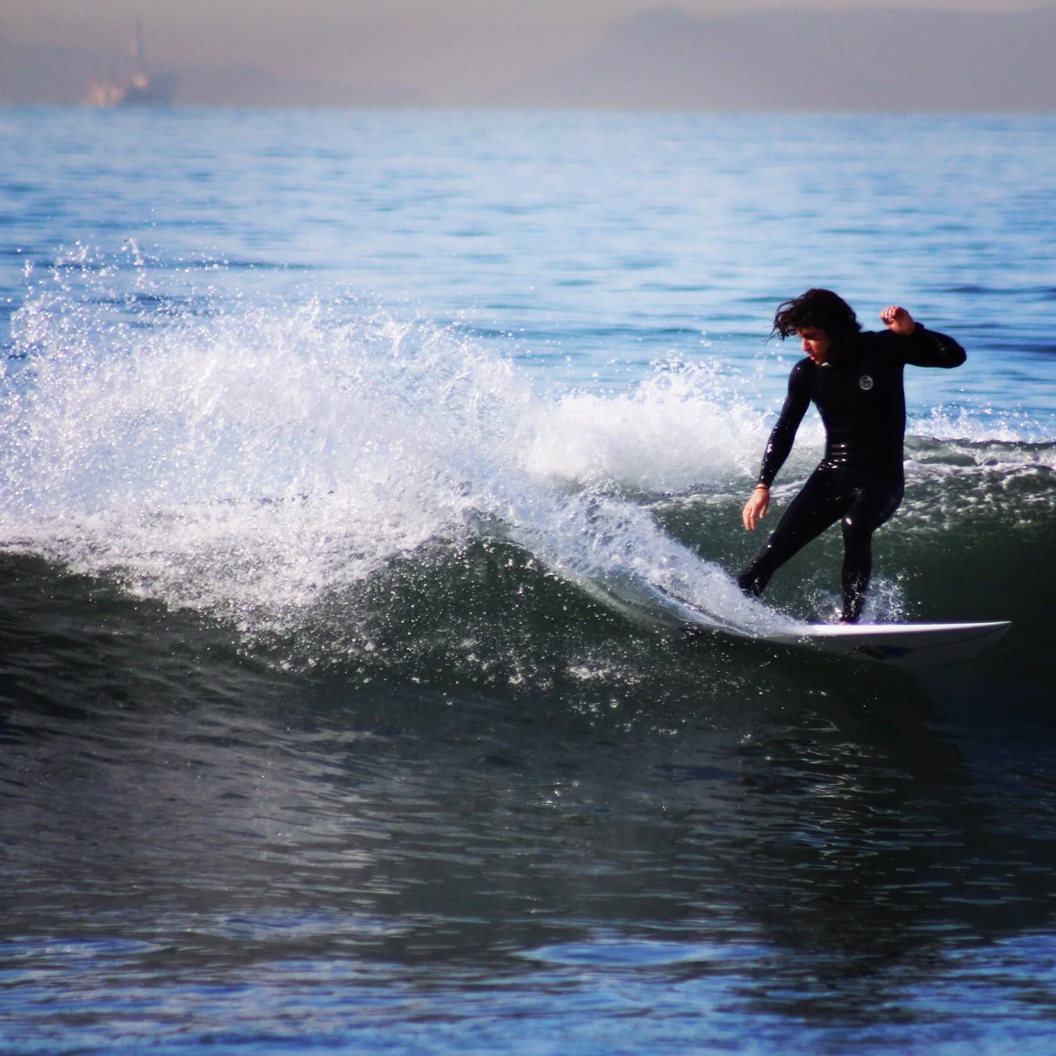 Vintage styled image in full color of a man in a solid black wetsuit surfing with a wave splashing up around him.