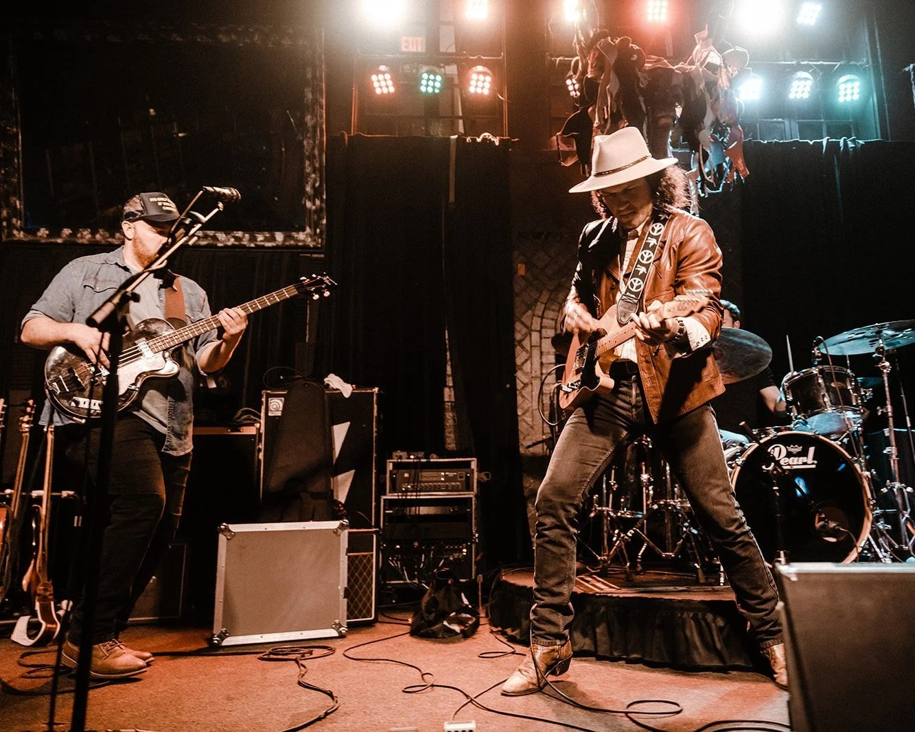 Two musicians on stage playing guitar with cowboy hats on and cowboy boots,
