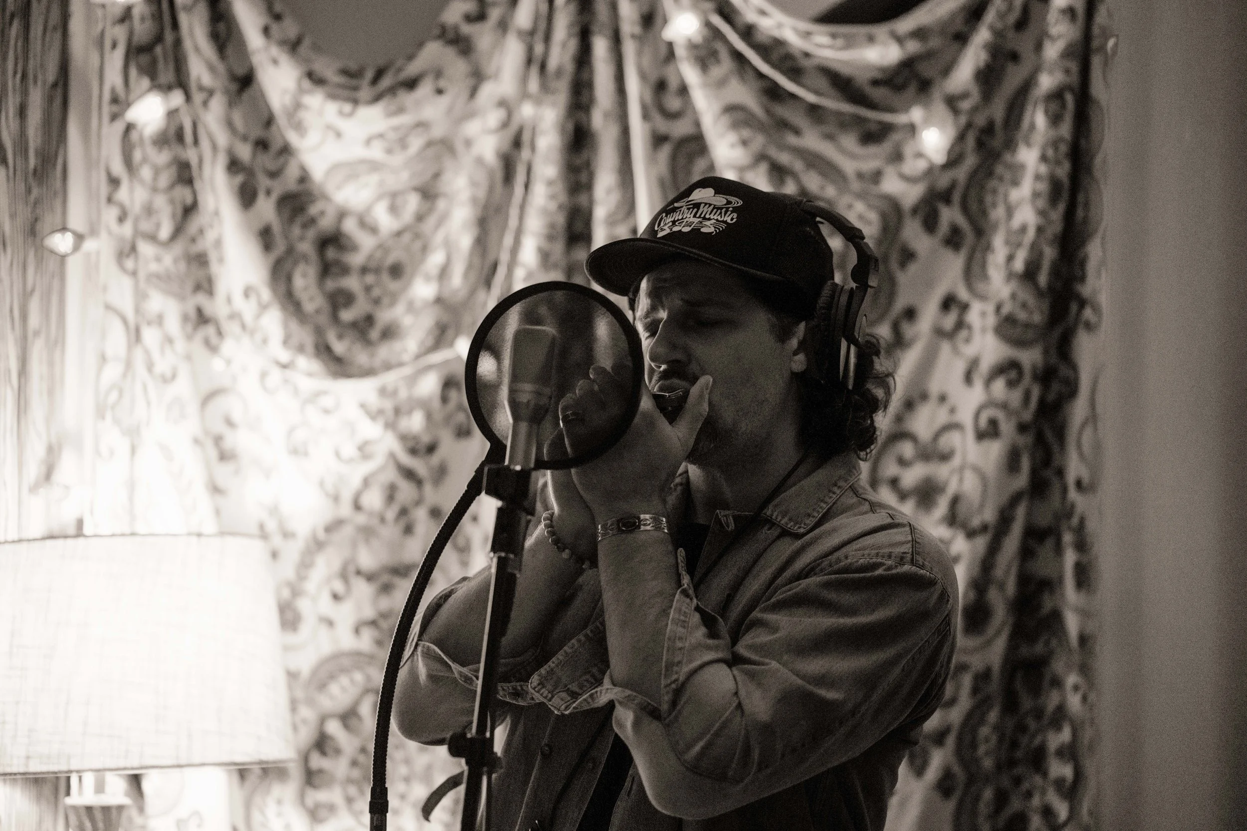 Country singer playing harmonica in a recording booth in a music studio. Image is black and white.