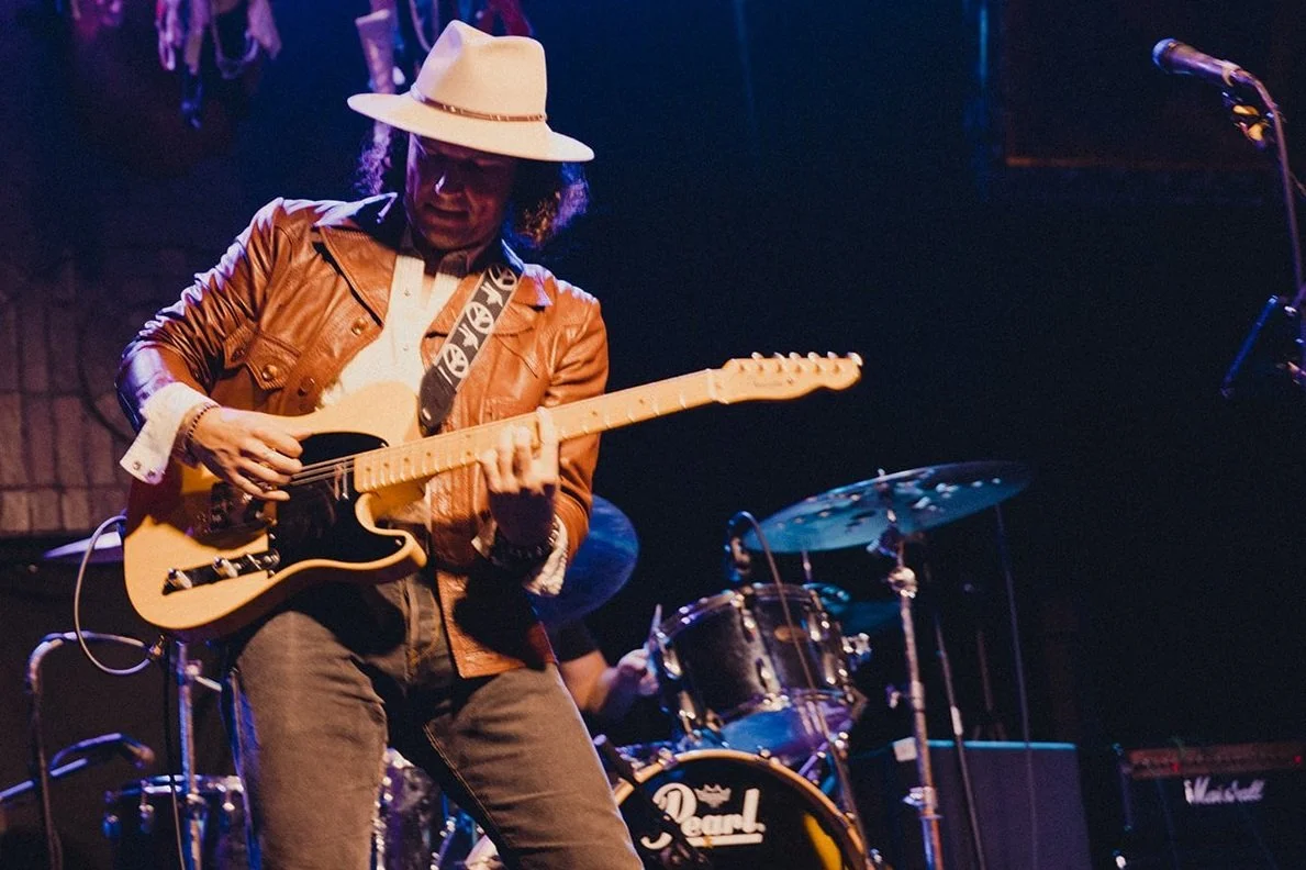 Country singer plays guitar on stage with blue lights on behind him.
