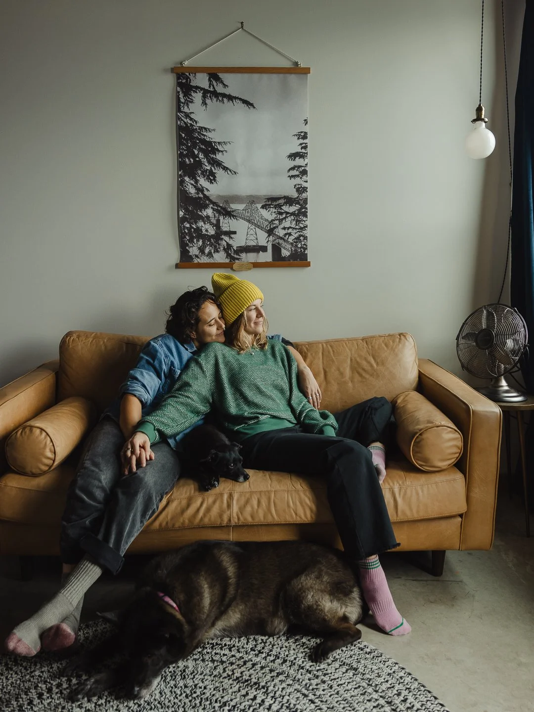 couple smiling on couch looking out window with dogs.